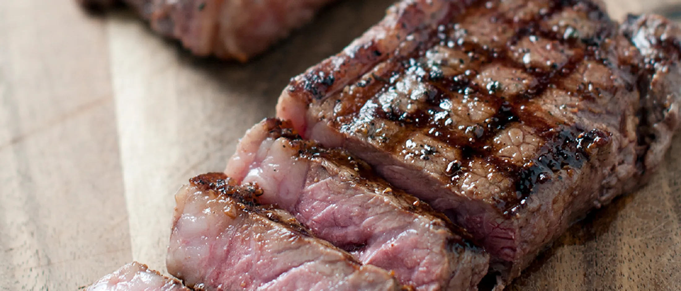 Grilled steak with caramelized surface, sliced on wooden board