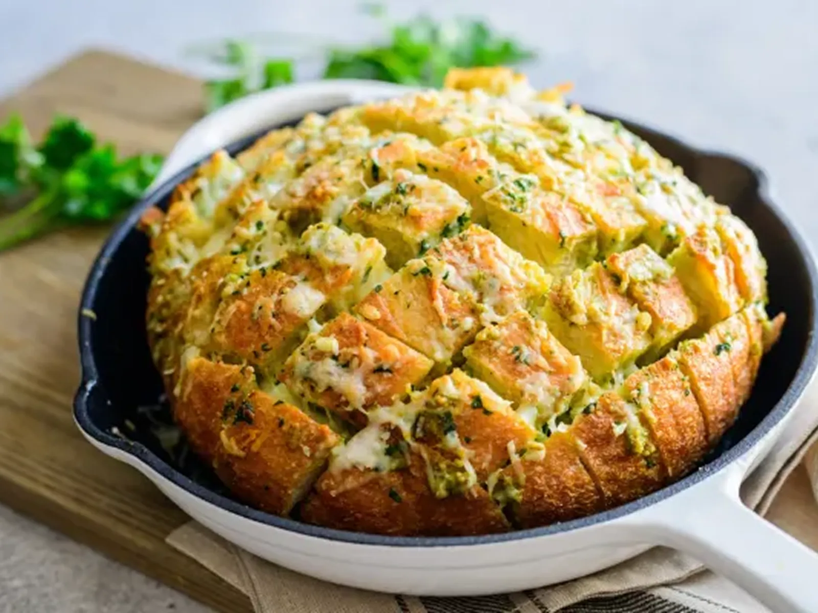 A round loaf of pesto and cheese bread, baked to golden perfection, sits in a white cast-iron pan.