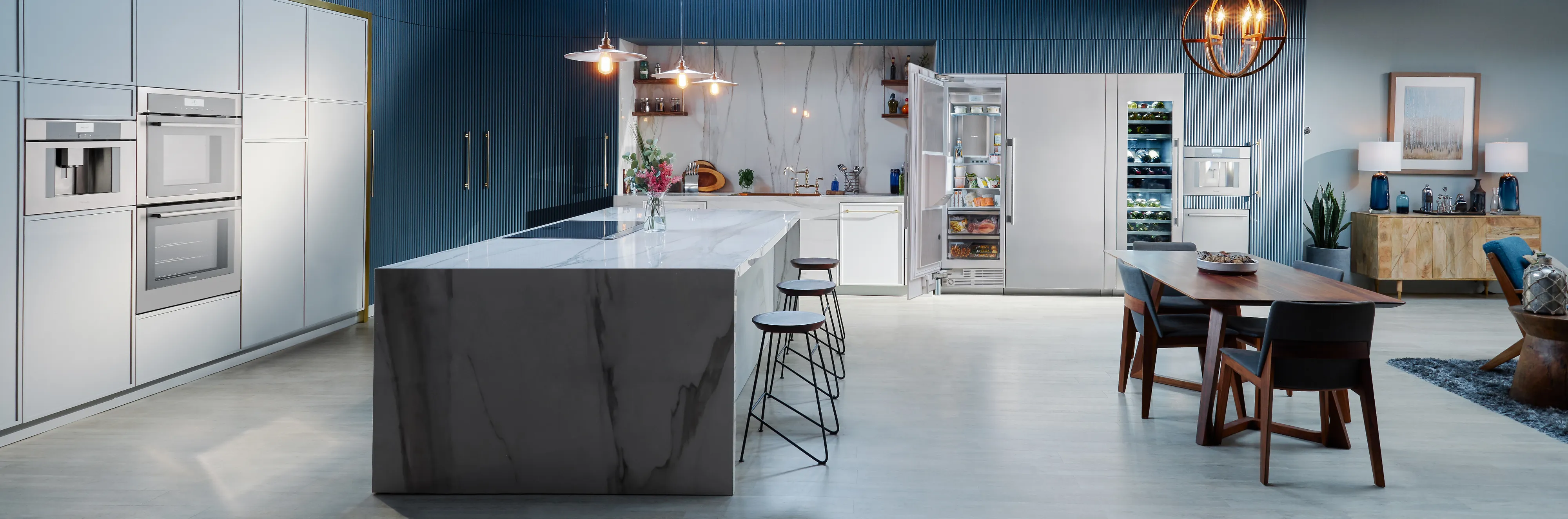 Modern open-concept kitchen and dining area with marble island, white cabinetry, blue accent wall, and wooden dining table with chairs.