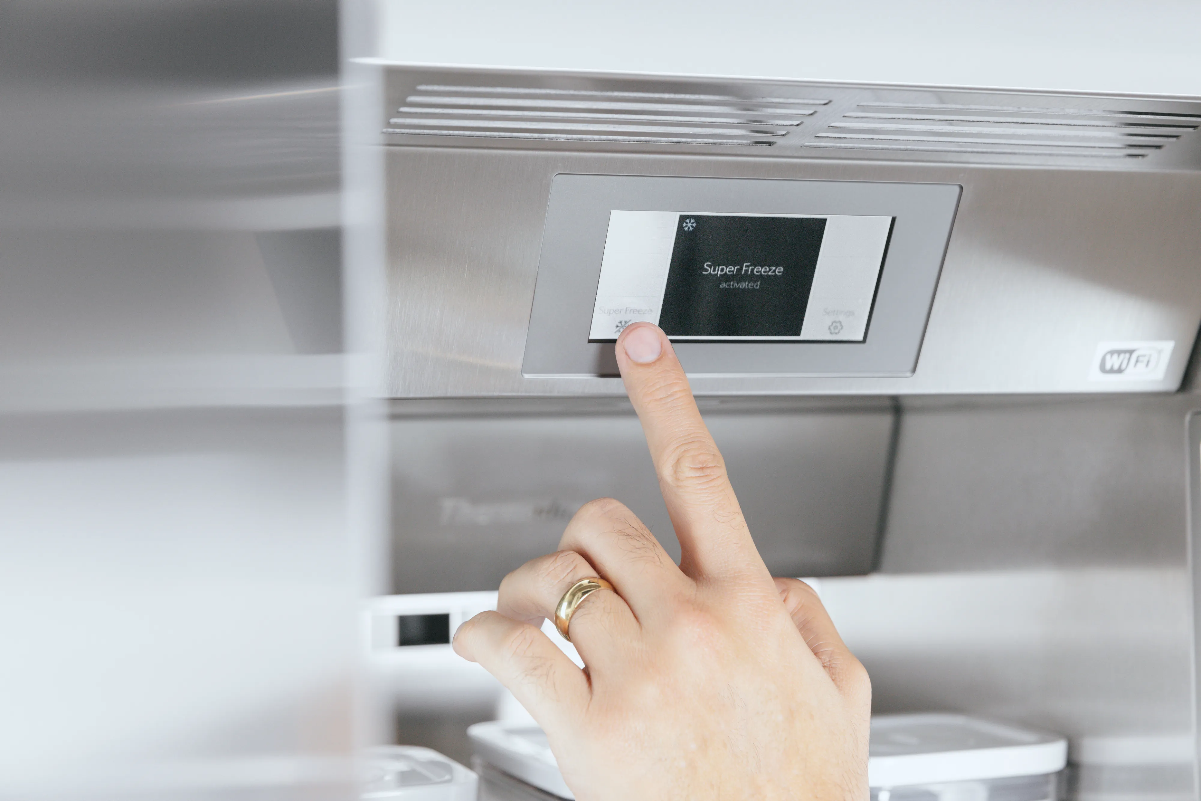 Hand pressing a touchscreen control panel on a modern stainless steel kitchen appliance.