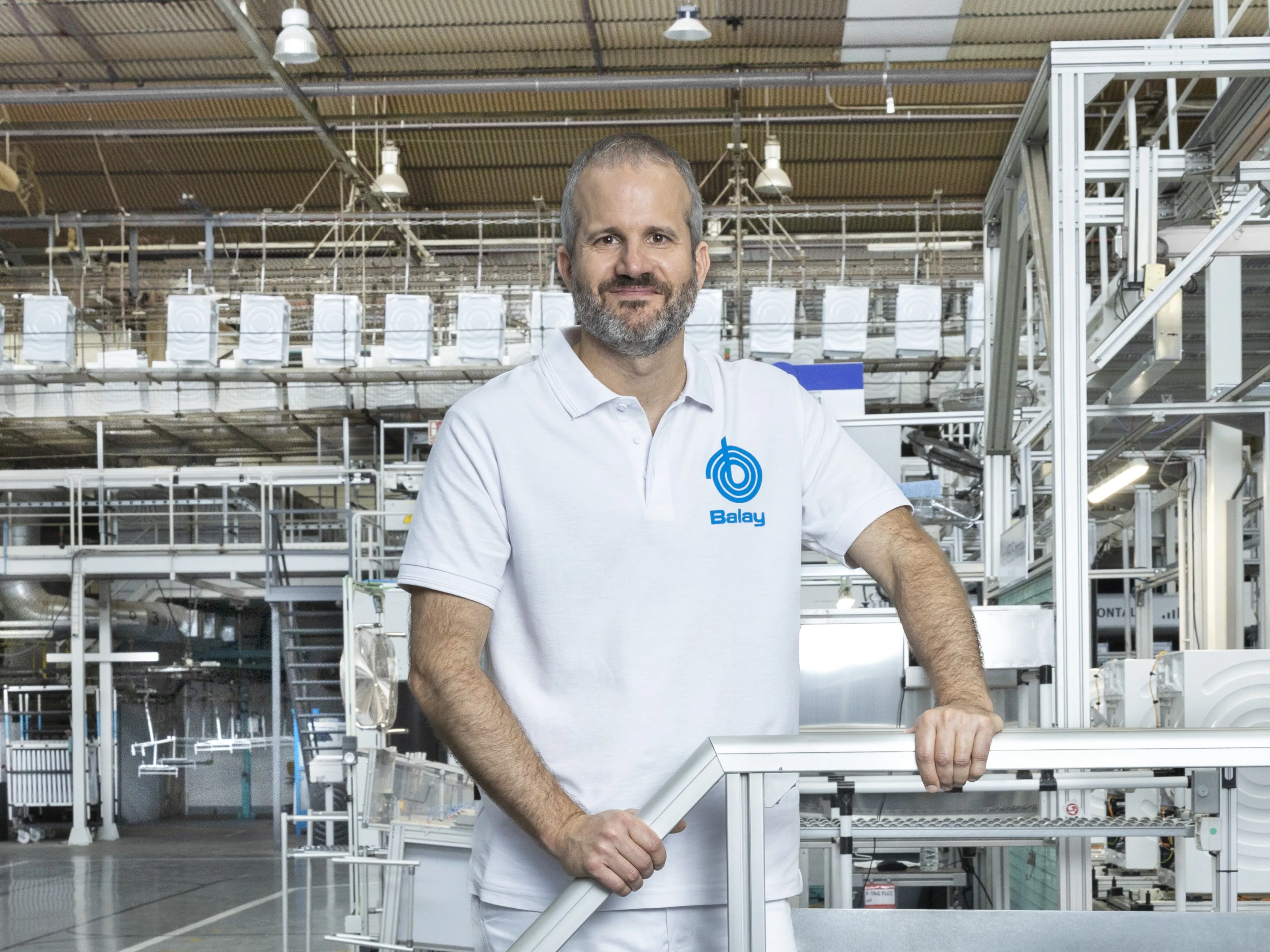 Trabajador con uniforme blanco de Balay de pie en una instalación de fabricación con equipos industriales al fondo