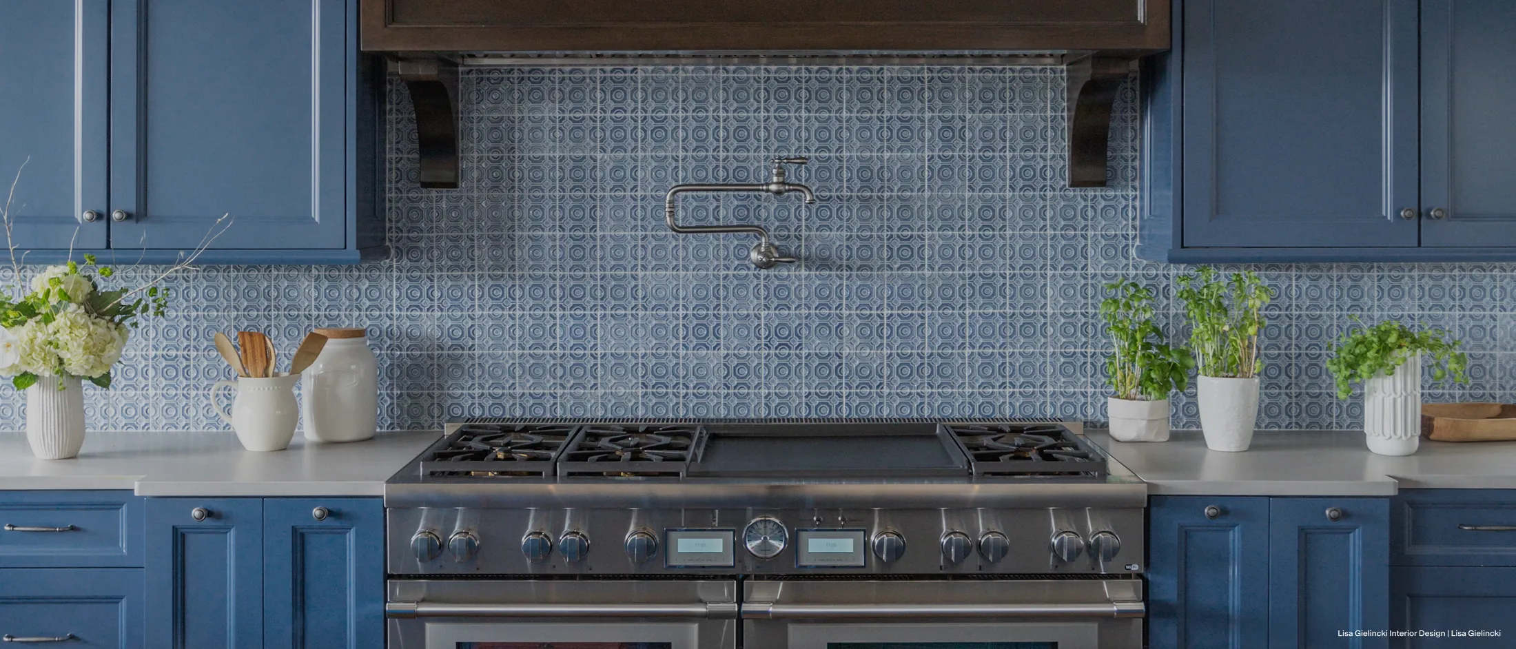 Modern kitchen with a stainless steel stove, blue cabinetry, blue patterned tile backsplash, and plants and flowers on the countertop.
