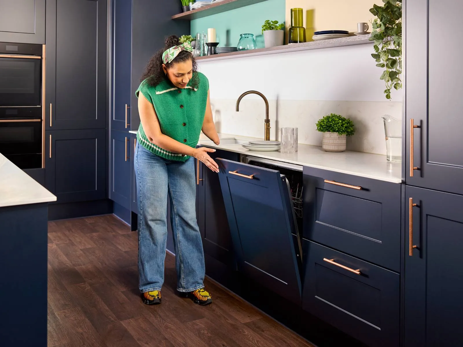 In a modern, blue kitchen, a woman with a limb difference effortlessly opens a dishwasher door with a light touch.