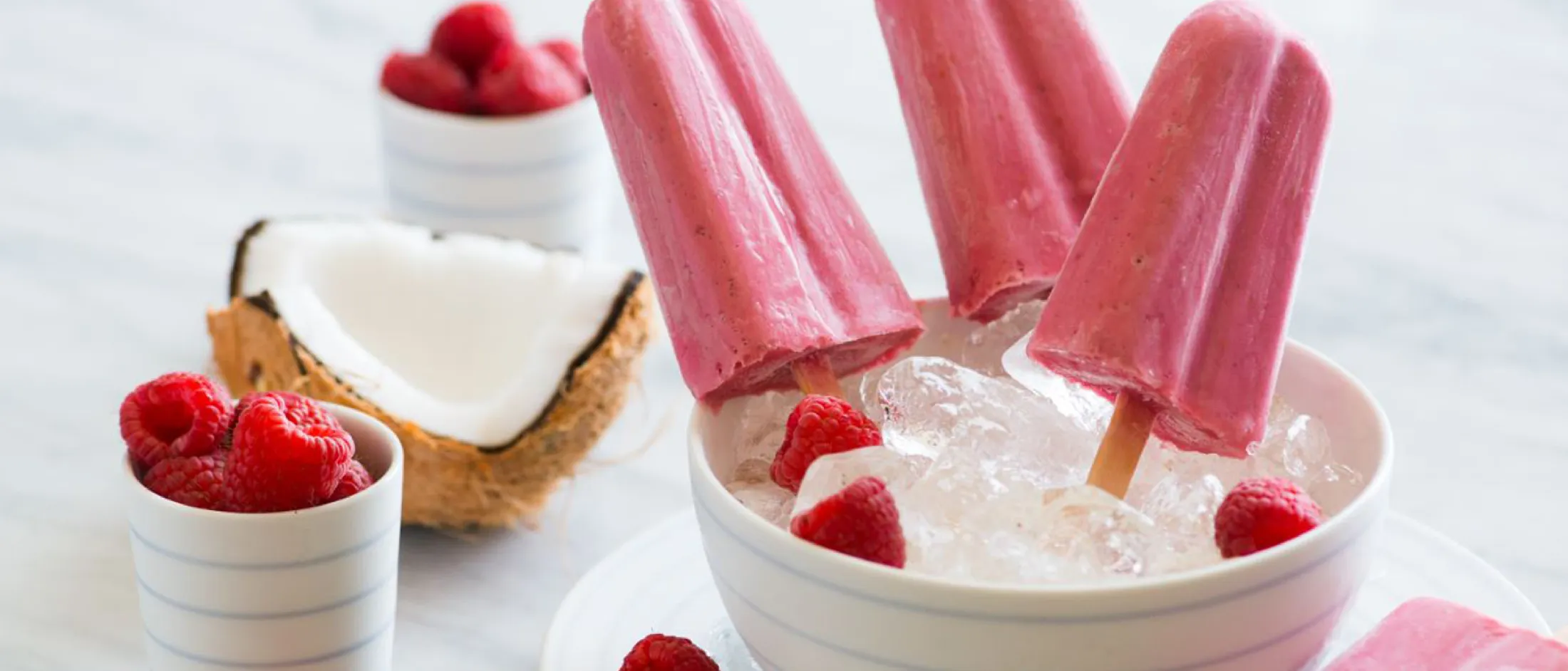 Strawberry popsicles, fresh strawberries, and coconut cream in white bowls on a light background