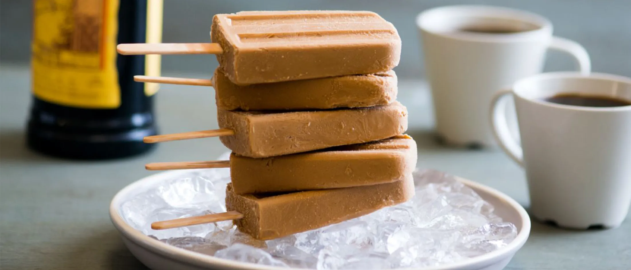 Stacked caramel bars on plate, coffee cups, and coffee beans on table