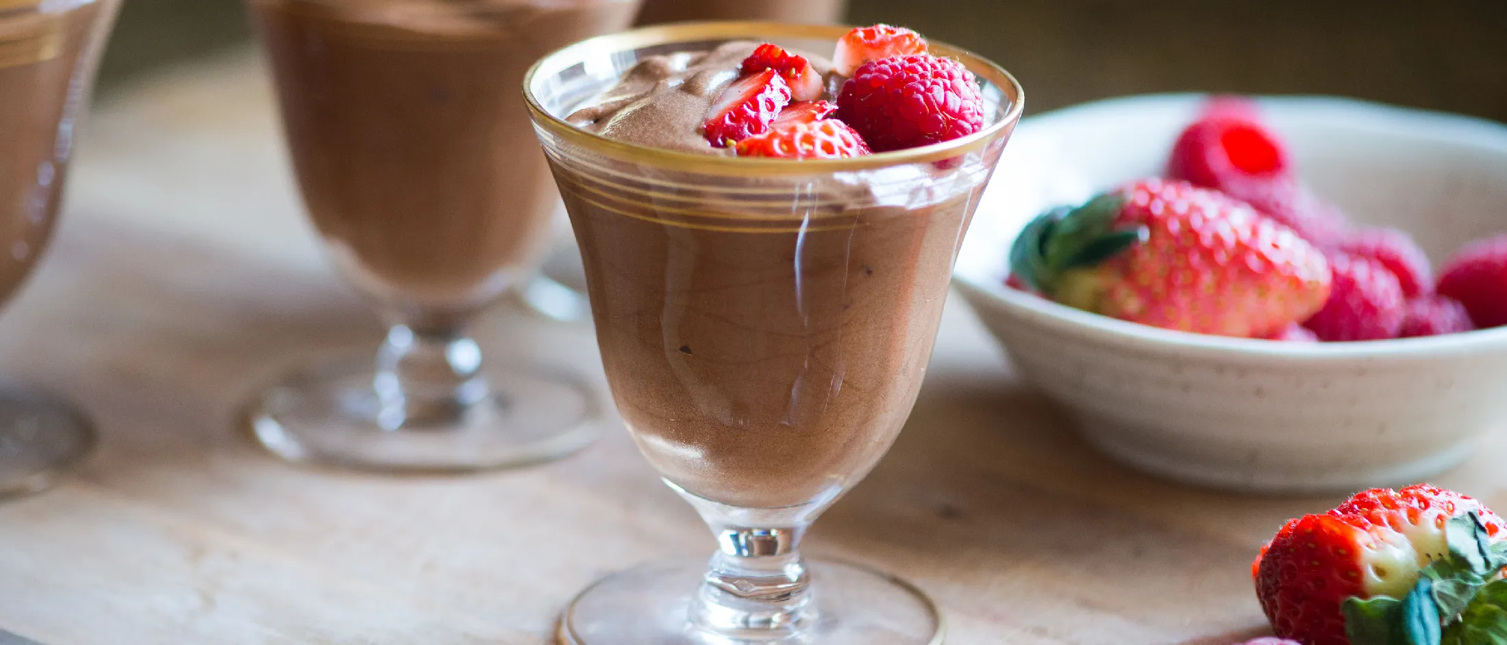 Chocolate mousse desserts with fresh strawberries in glass cups on a wooden table
