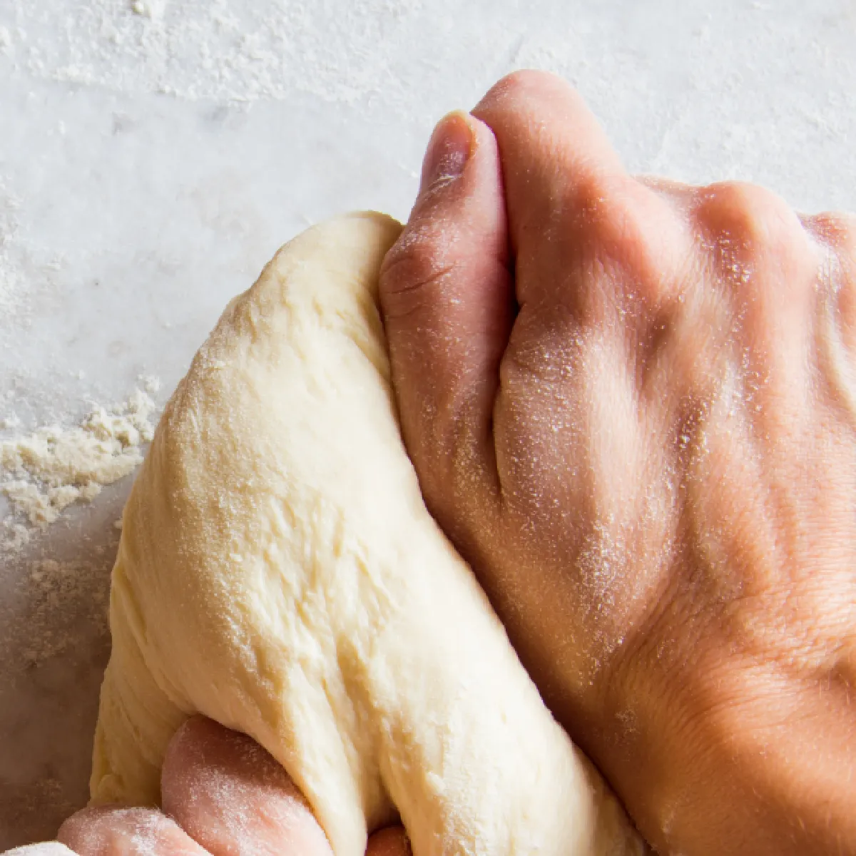 A person kneads a ball of dough on a floured surface.