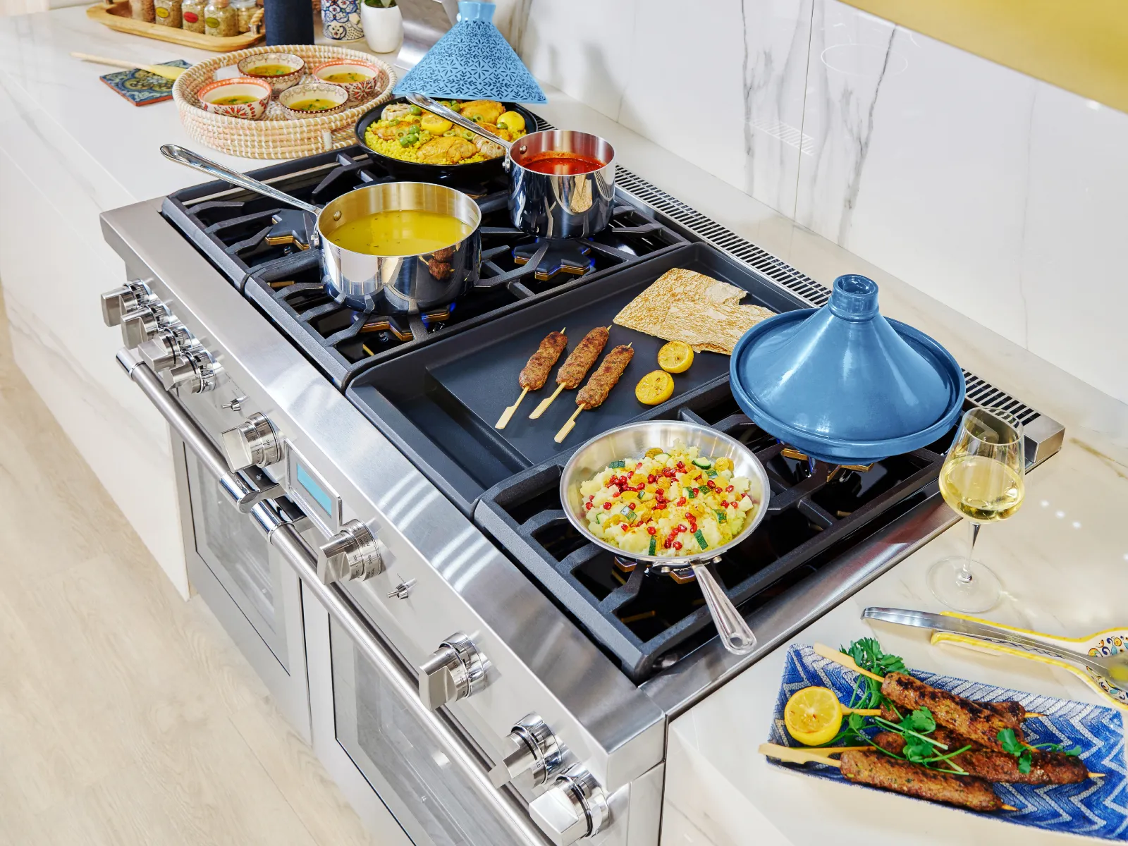 A stainless steel range with multiple dishes cooking on the stovetop, including kebabs, soup, and rice, set in a modern kitchen with marble countertops.