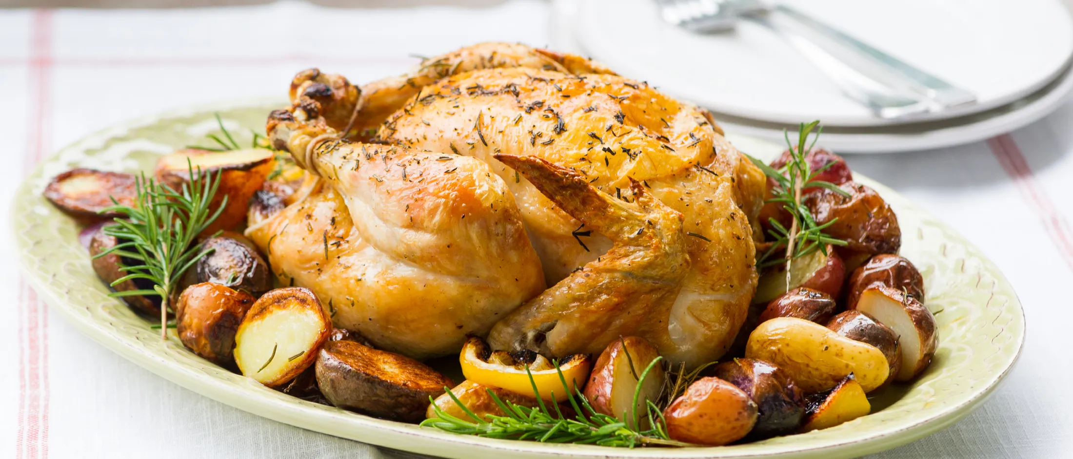 Roasted whole chicken garnished with rosemary and served with assorted roasted potatoes on a green platter.