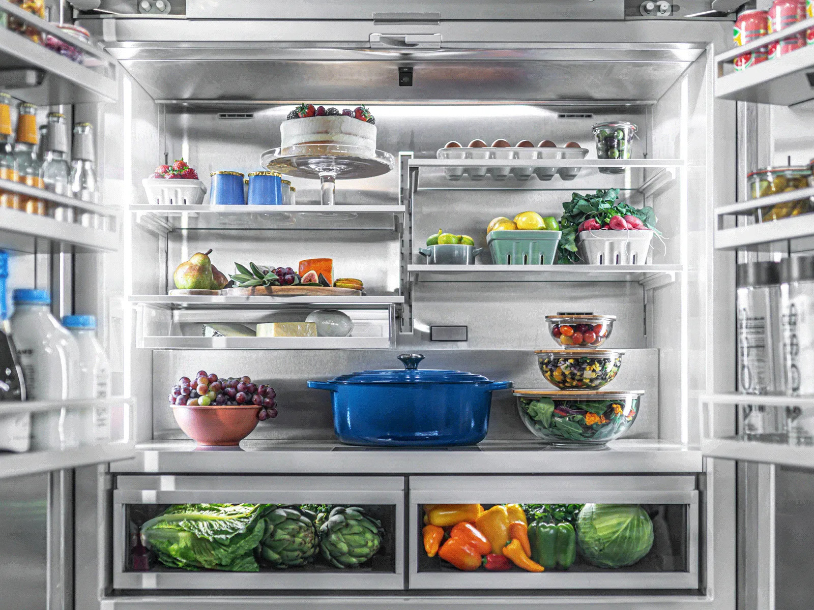 Open stainless steel refrigerator filled with fresh food, including fruits, vegetables, and a cake.