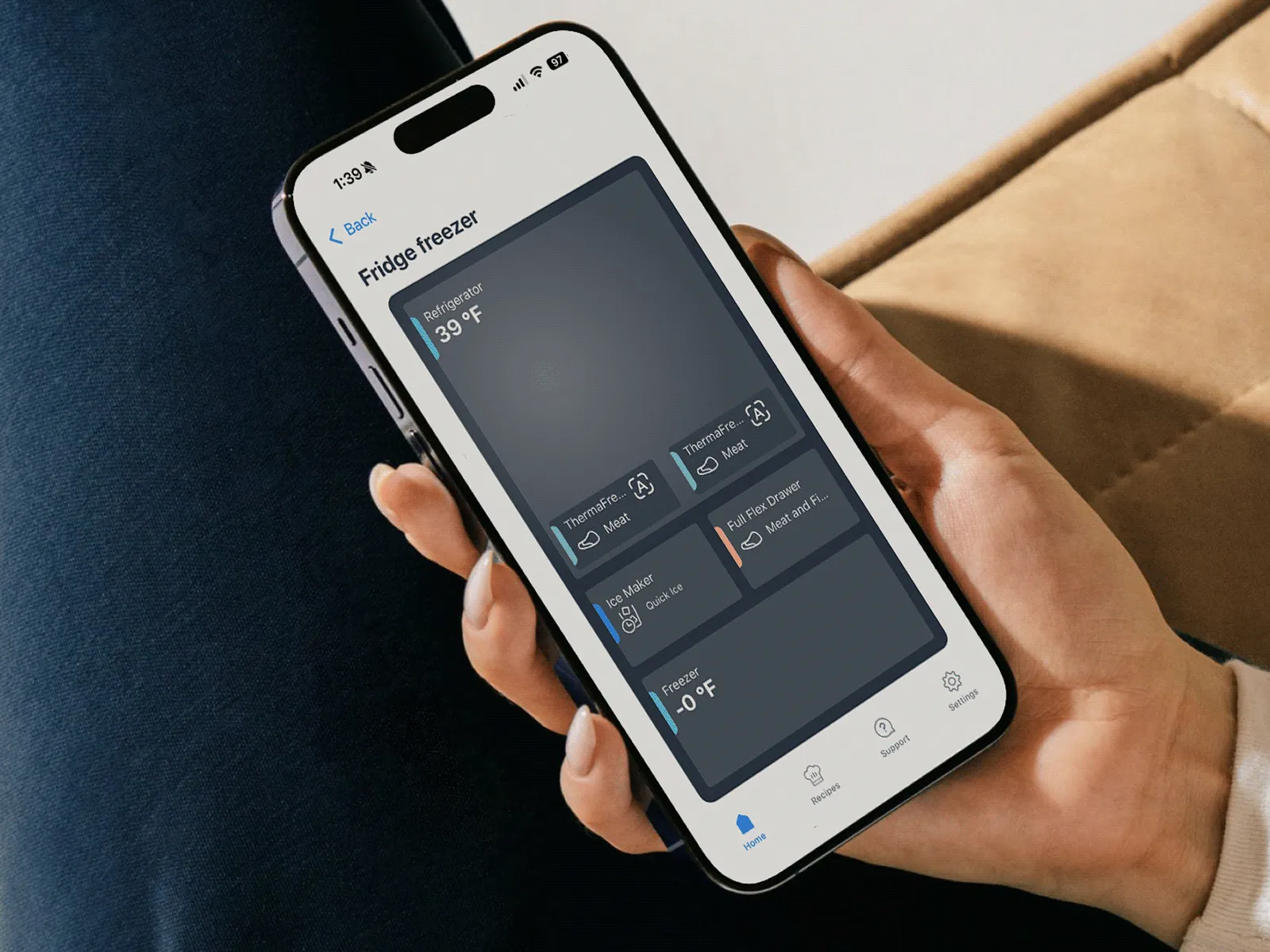Hand holding a smartphone displaying a "Fridge freezer" app interface with temperature readings.