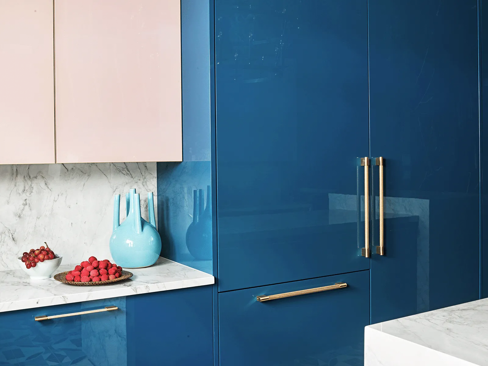 Modern kitchen with glossy blue cabinets, marble countertop, and pink upper cabinets.