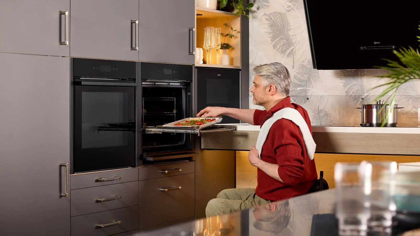 A wheelchair user puts a tray of vegetables on a Flexi Rail shelf. The shelf has been pulled fully out of the oven for convenience and safety.
