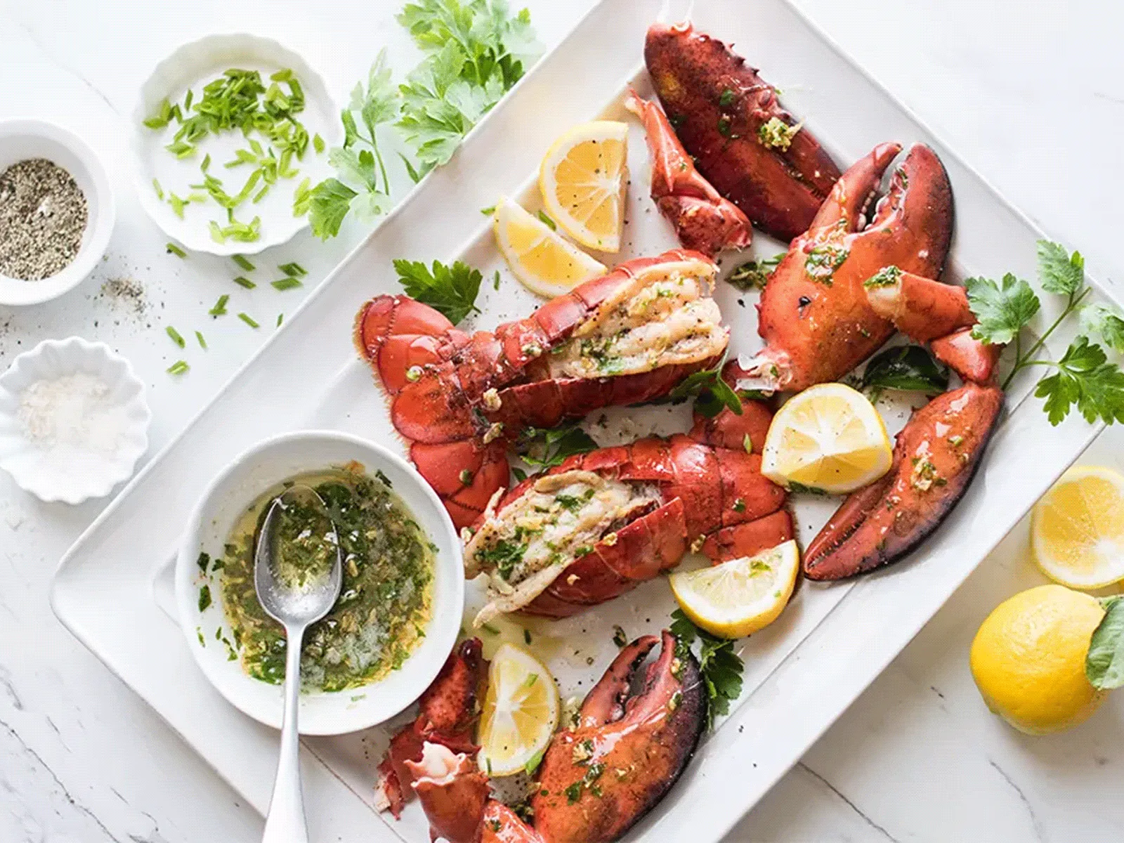 Platter of split cooked lobster claws with lemon wedges and herb butter sauce.
