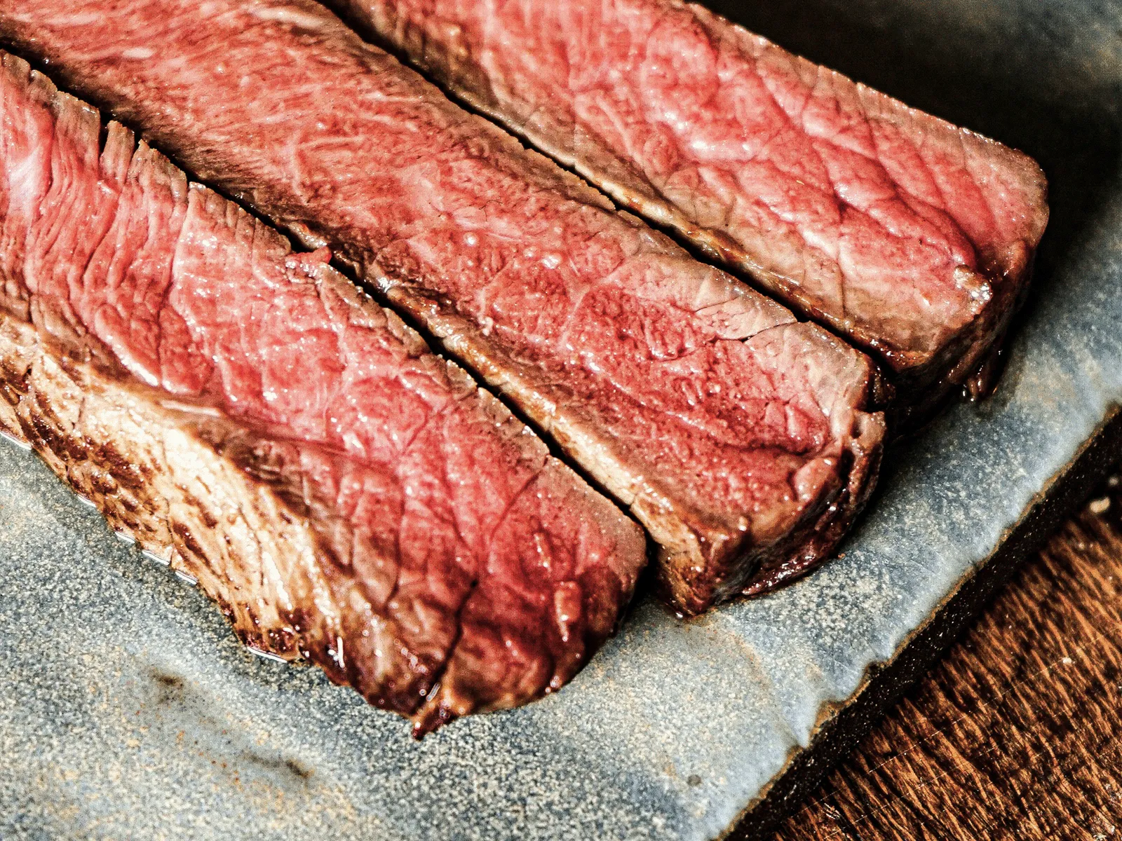 Close-up of three slices of medium-rare cooked steak on a textured ceramic plate.