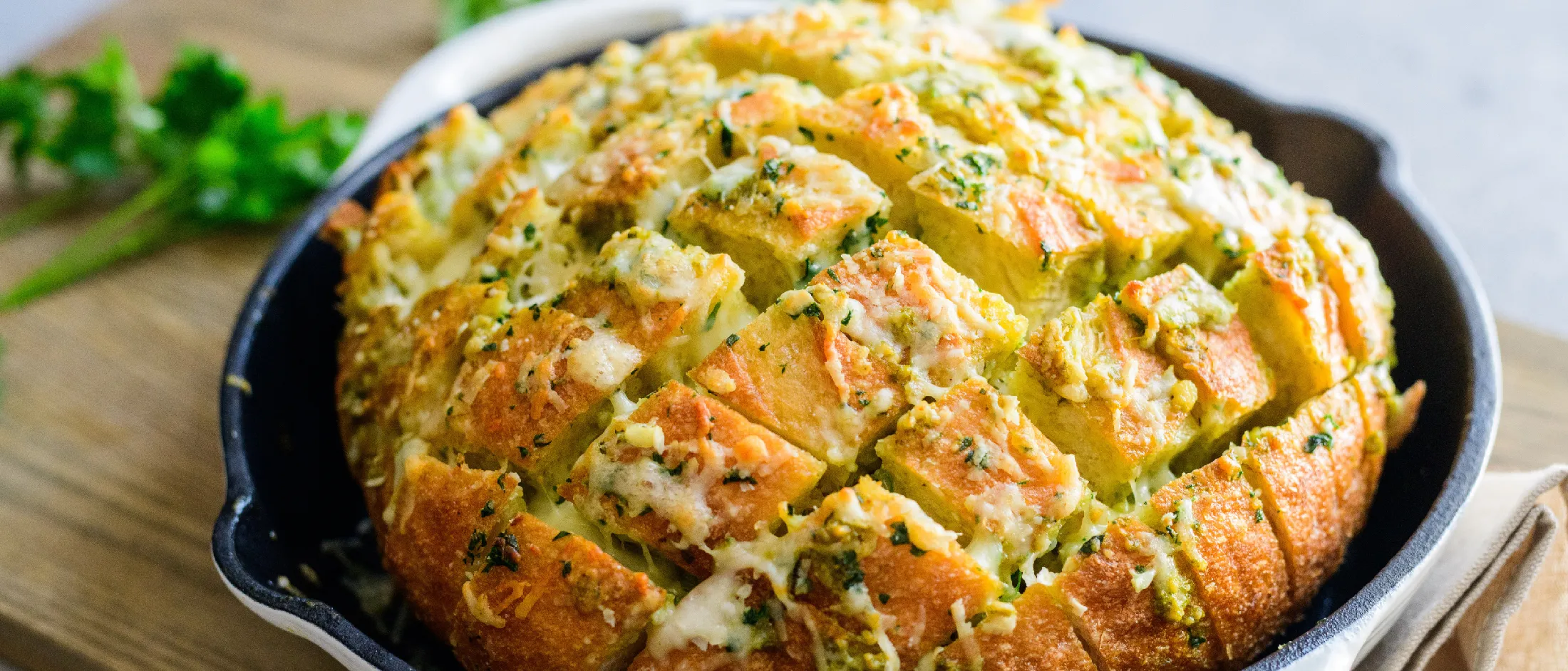 Round loaf of pull-apart bread with herb and cheese filling in a cast-iron skillet on a wooden board.