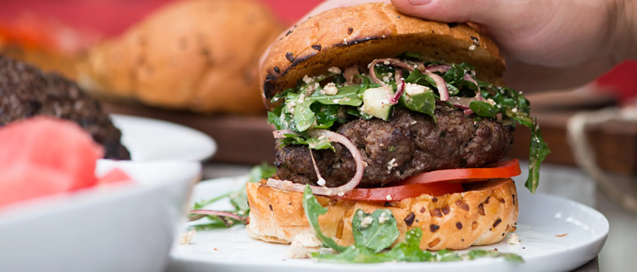 Juicy burger with fresh greens, tomato, and onion on a toasted bun, served on a white plate.