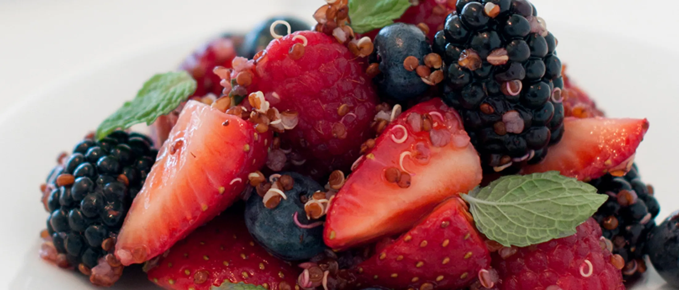 Close-up of a fresh fruit and quinoa salad with strawberries, raspberries, blackberries, blueberries, and mint leaves