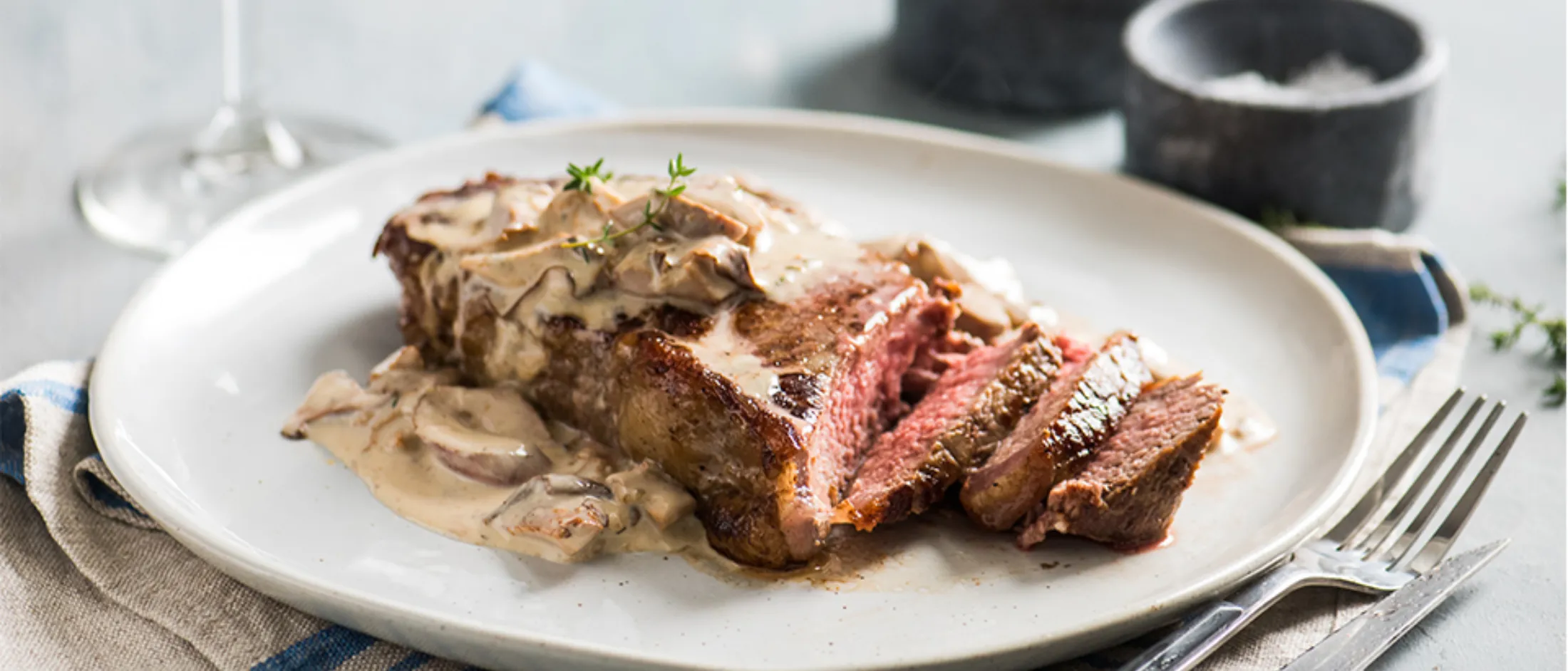 Seared steak with mushroom sauce, red wine, and garnish on a white plate.