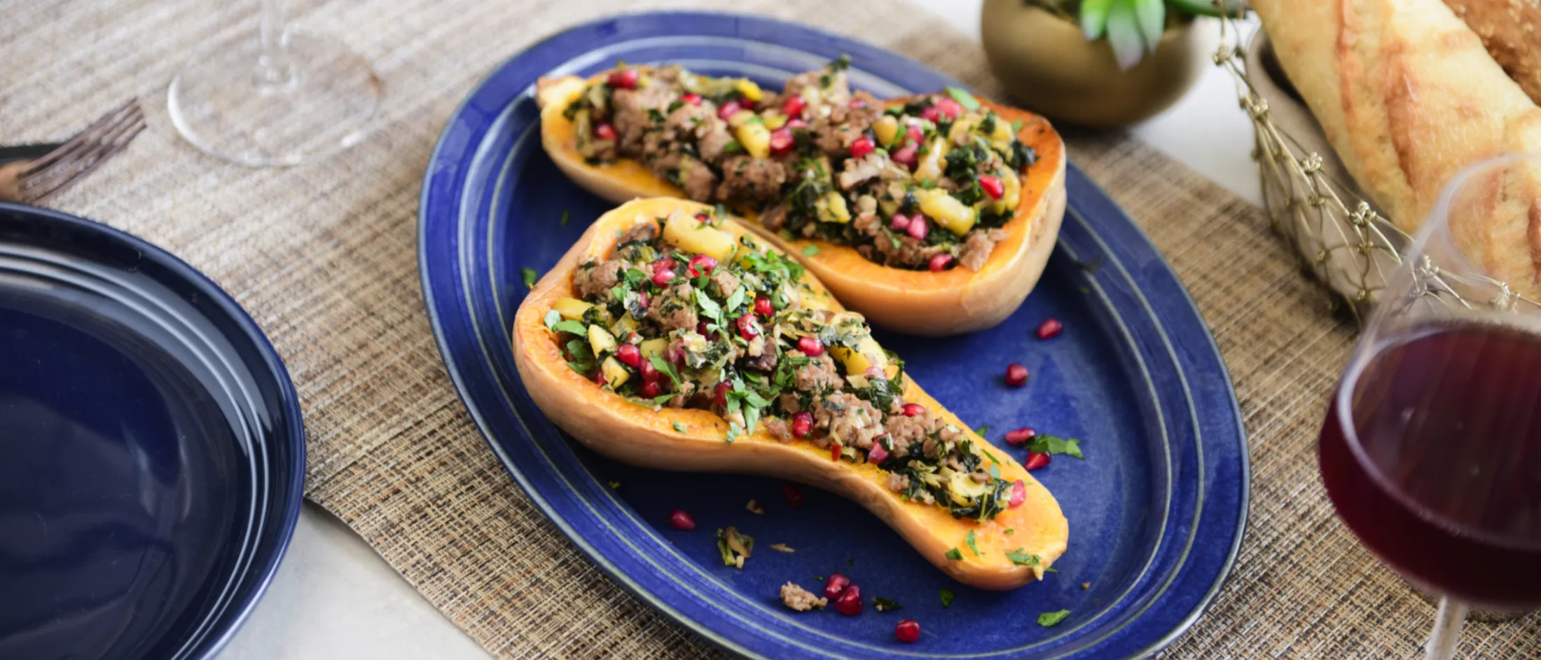 Two halves of stuffed butternut squash on a blue oval plate with pomegranate seeds on top