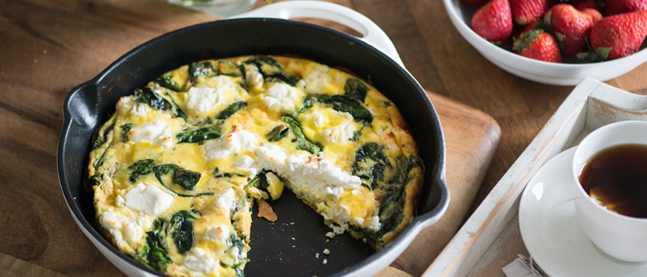 Frittata with spinach, eggs, and cheese, served with fresh strawberries and a cup of coffee.