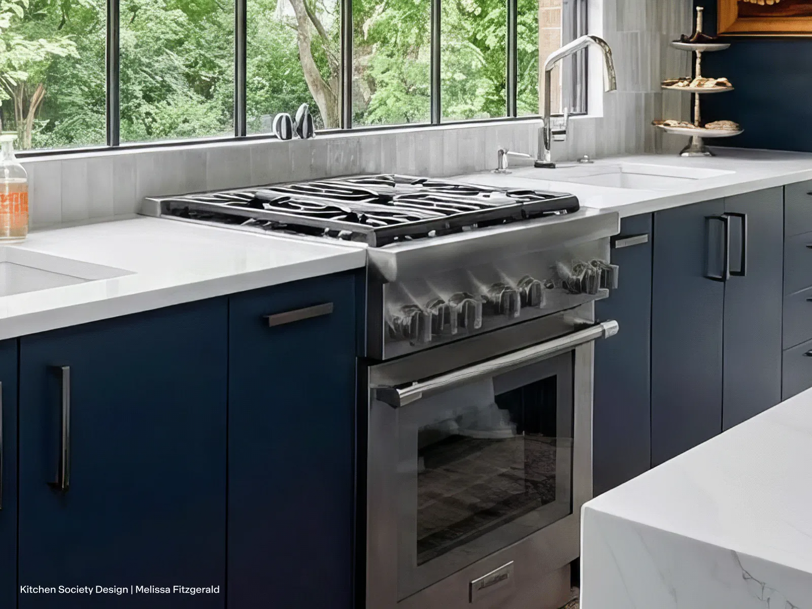 A stainless steel Thermador gas range is installed in a sophisticated, modern kitchen featuring deep navy blue cabinets and crisp white countertops. A large window behind the cooktop offers a view of lush green trees, adding a natural element to the sleek design.
