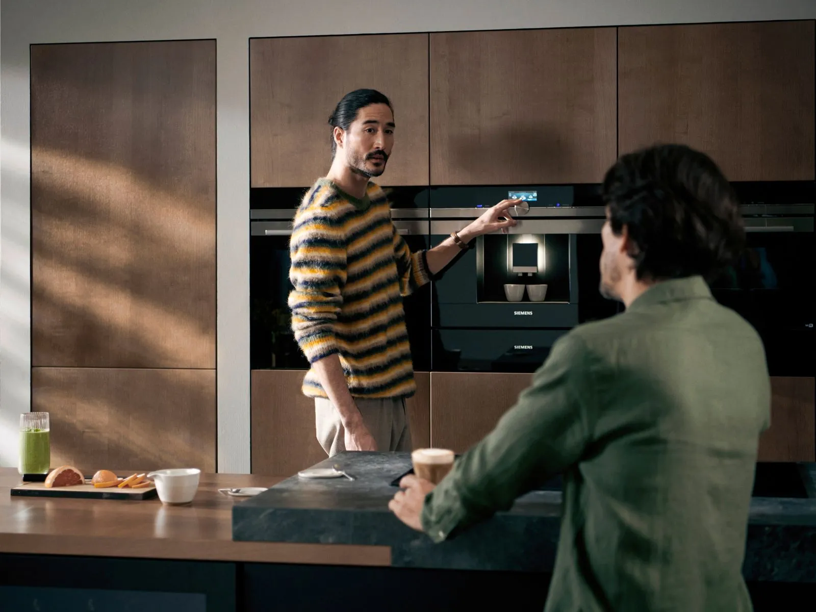 Person operating a Siemens built-in coffee machine integrated into a modern wooden kitchen cabinet.