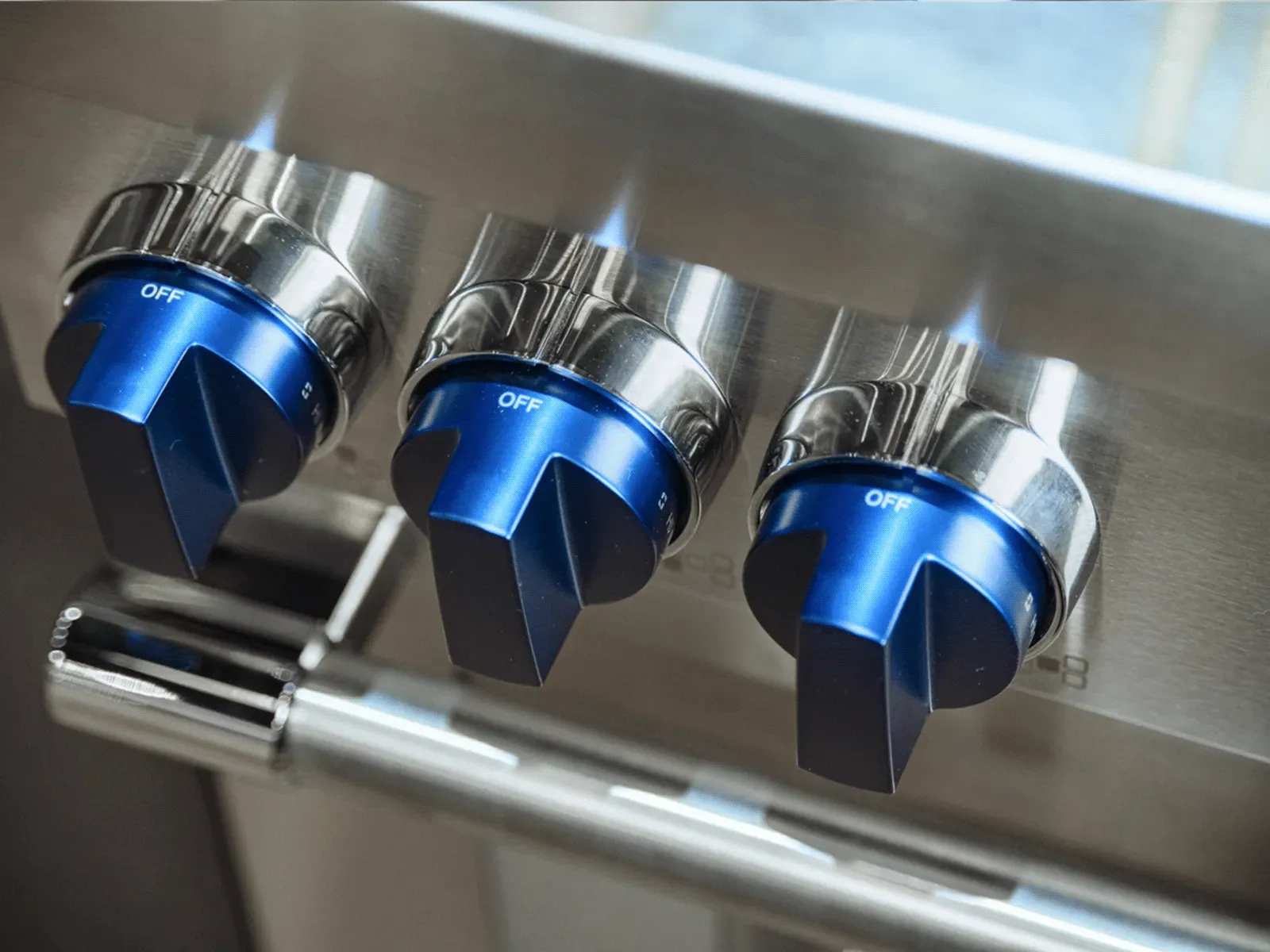 Close-up of three blue gas stove knobs set to off on a stainless steel stovetop.