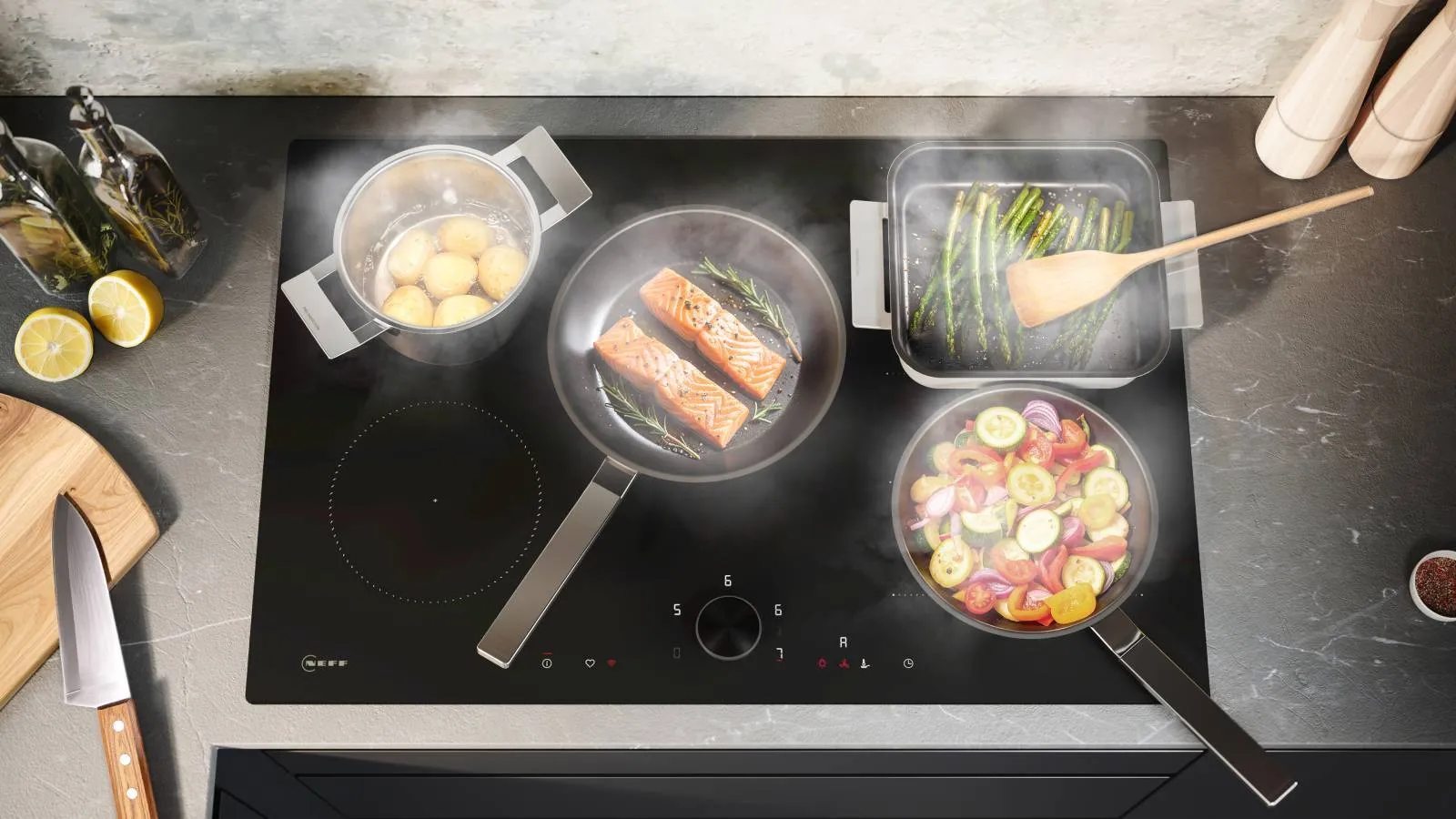 An overhead view of a black induction cooktop in action, with various pots and pans cooking salmon, potatoes, asparagus, and mixed vegetables simultaneously.