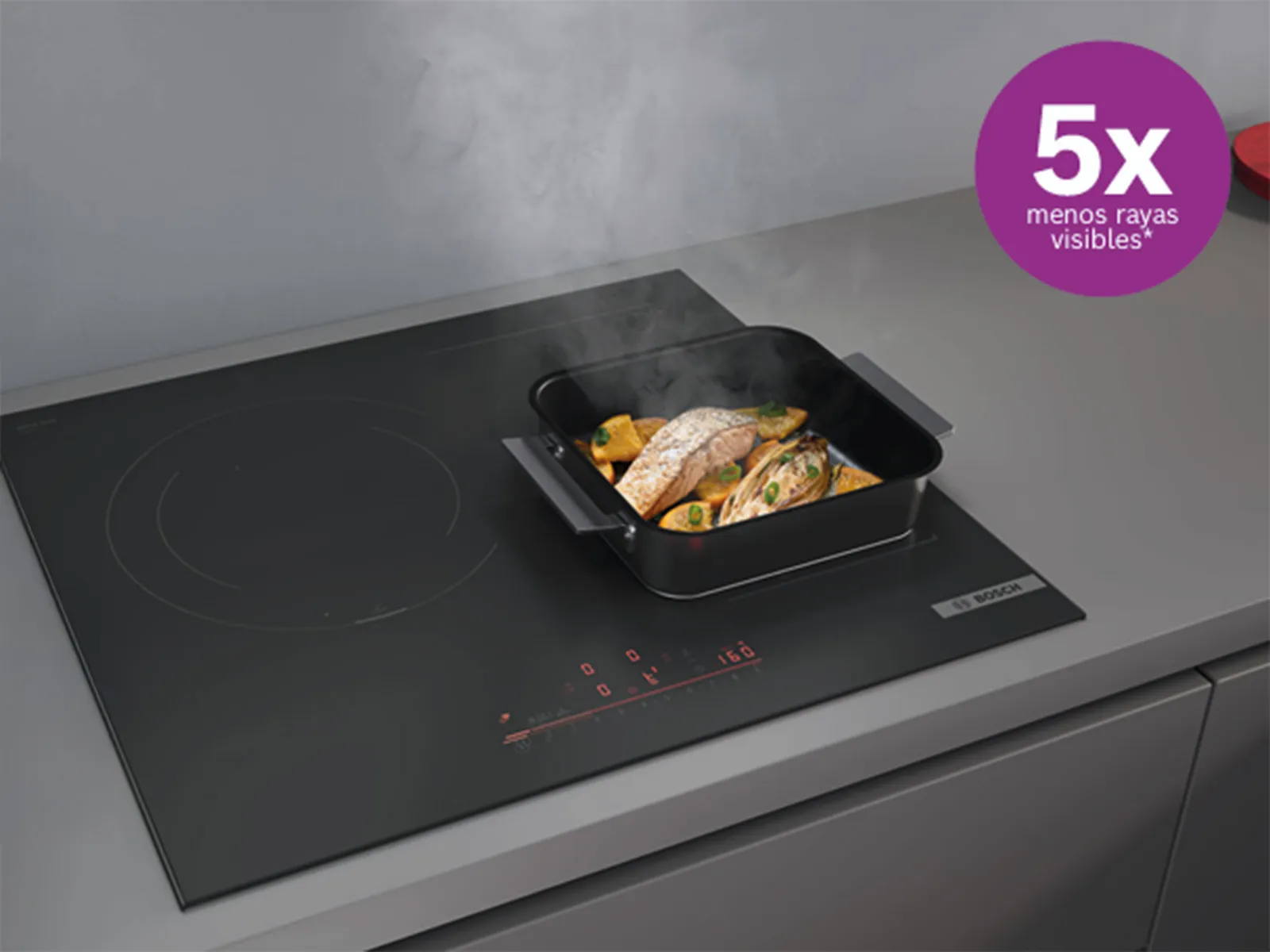 Una placa de inducción negra con una olla de pescado y verduras cocinándose, emitiendo vapor. Una etiqueta morada en la esquina dice "5x menos rayas visibles".