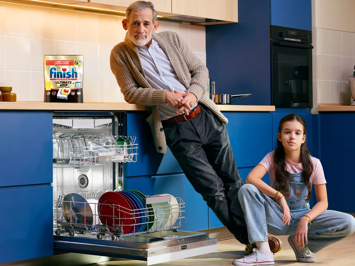Adult and child in kitchen next to open Dishwasher with Finish pack on top