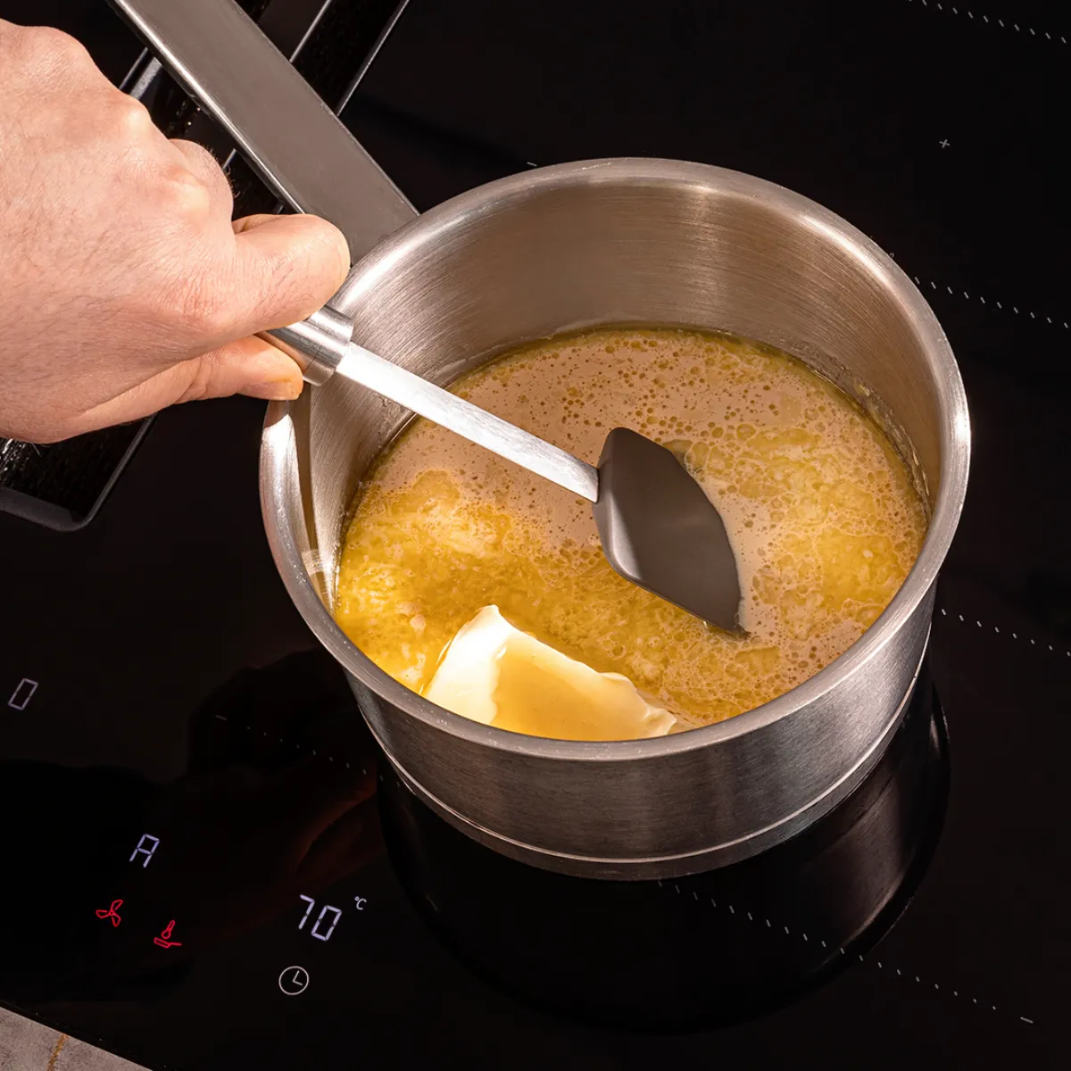Cooking on stove, hand stirring pot with liquid, kitchen appliance, cooking utensil, food preparation.