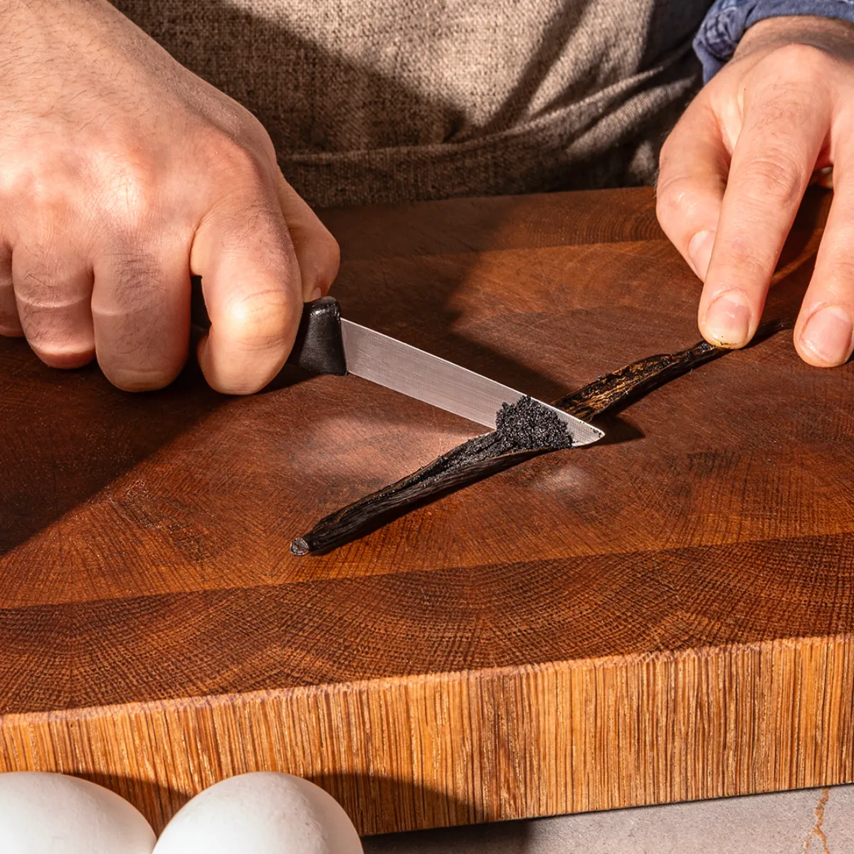 Hands chopping ingredients on a wooden cutting board, including eggs and spices, for cooking or baking.