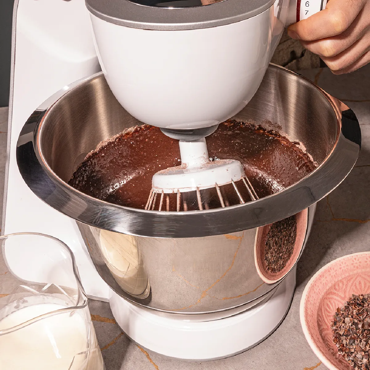 Coffee grinder with ground coffee beans, milk, and other ingredients on kitchen counter.
