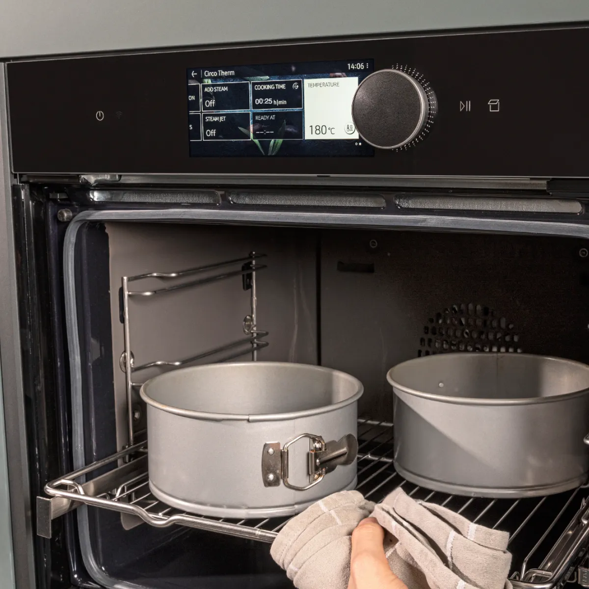 Oven interior with baking dishes, kitchen utensils, and a hand visible adjusting the oven controls.