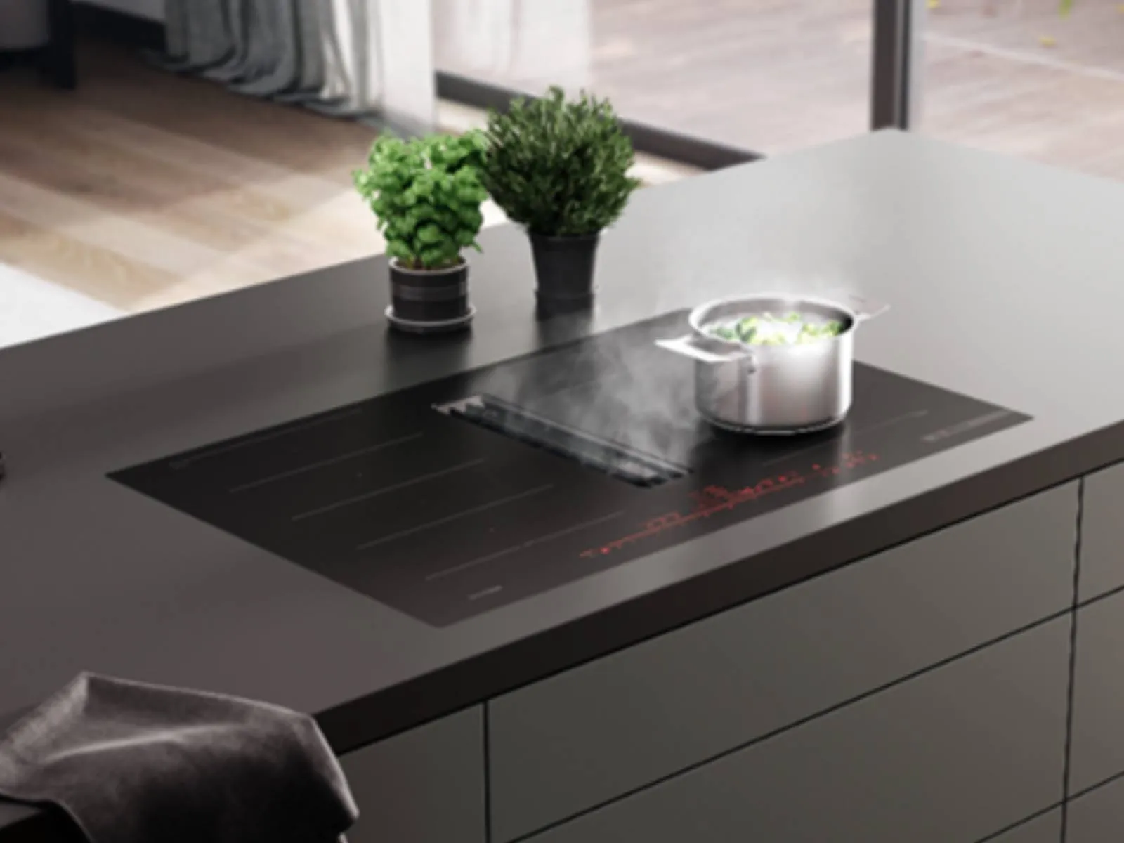 A black Bosch induction cooktop with an integrated downdraft extractor actively pulling steam from a pot of broccoli, set in a modern kitchen island.