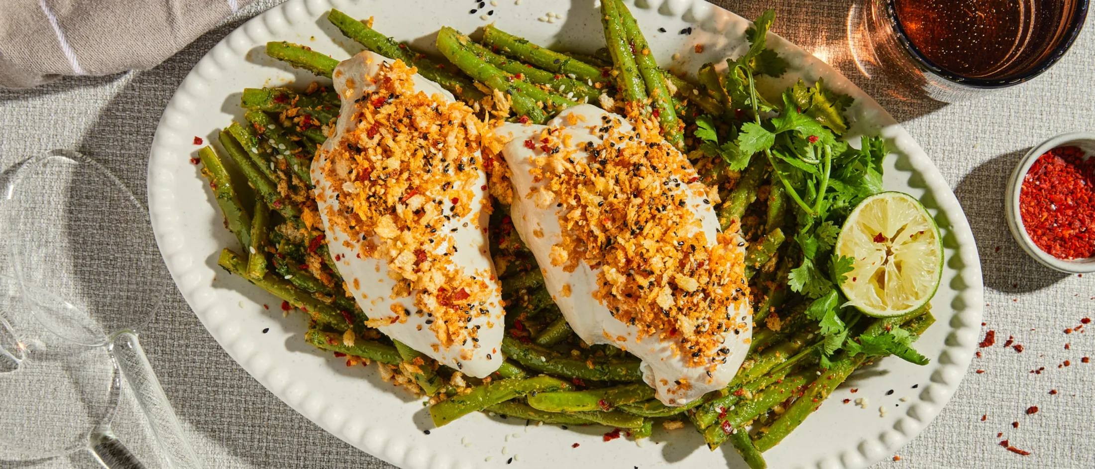 Zwei Stücke Weißfisch mit knuspriger Panade und schwarzem Sesam, serviert auf grünen Bohnen mit Limette und Koriander.