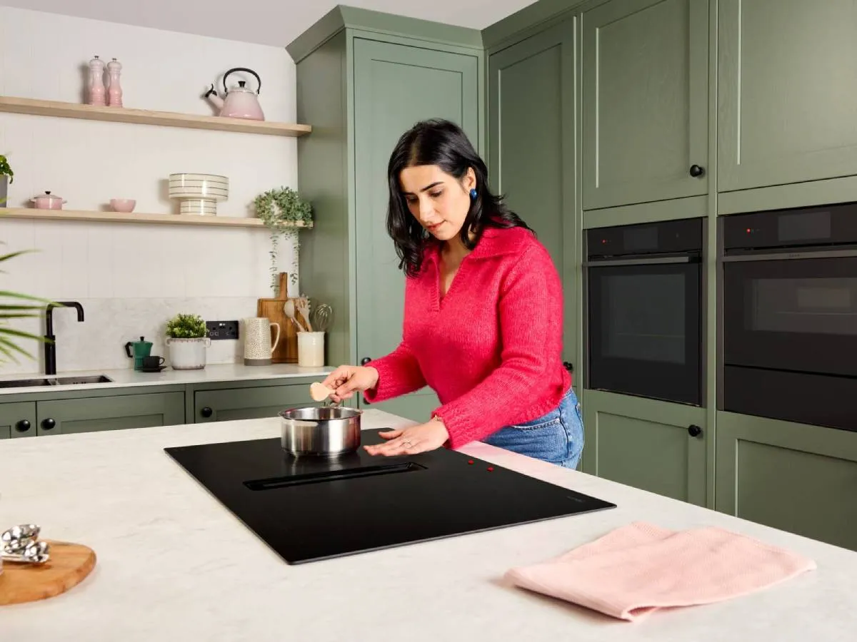 A woman with low vision stands at an induction hob. Her hand hovers safely over the hob, due to low residual heat after cooking.