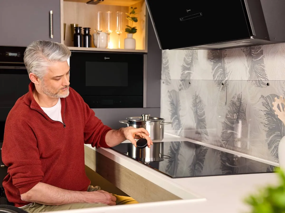 A wheelchair user holding a removable Twist Pad dial above an induction hob