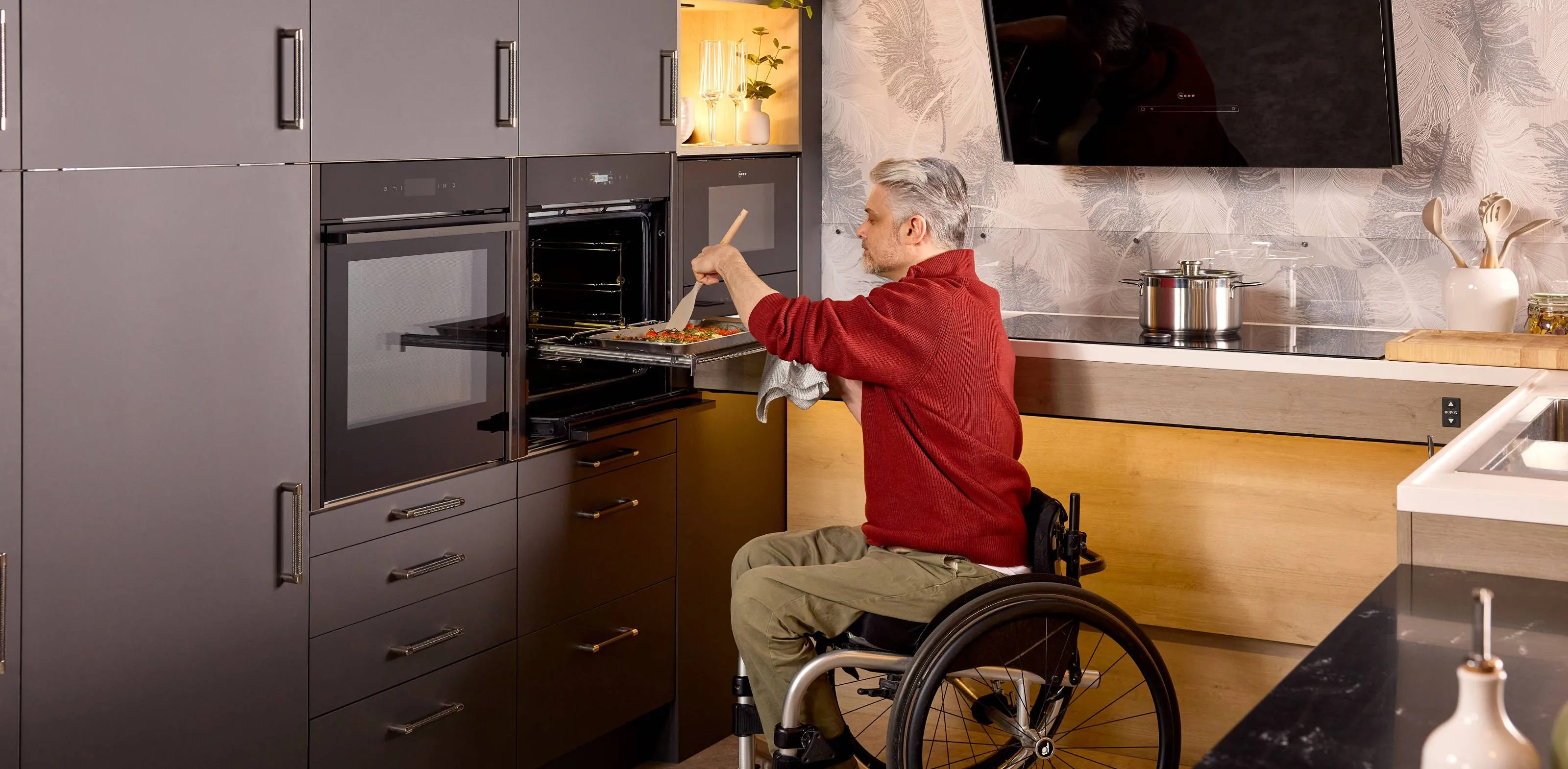 A wheelchair user effortlessly stirs a tray of roasted vegetables. The tray sits on the fully extended Flexi Rail for convenience and safety.