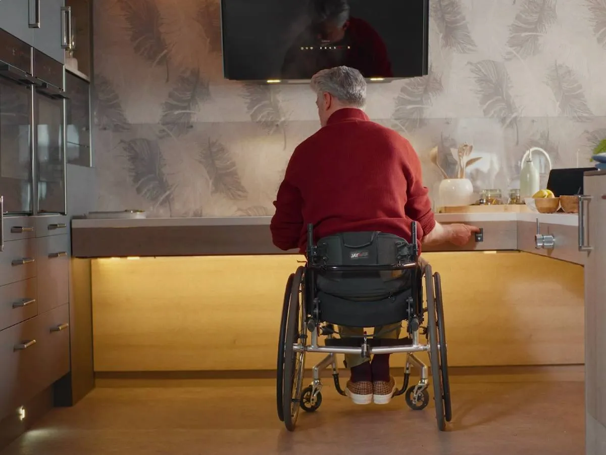 A wheelchair user next to a worktop, adjusting a rise and fall worktop to reach the optimal height of the hob.