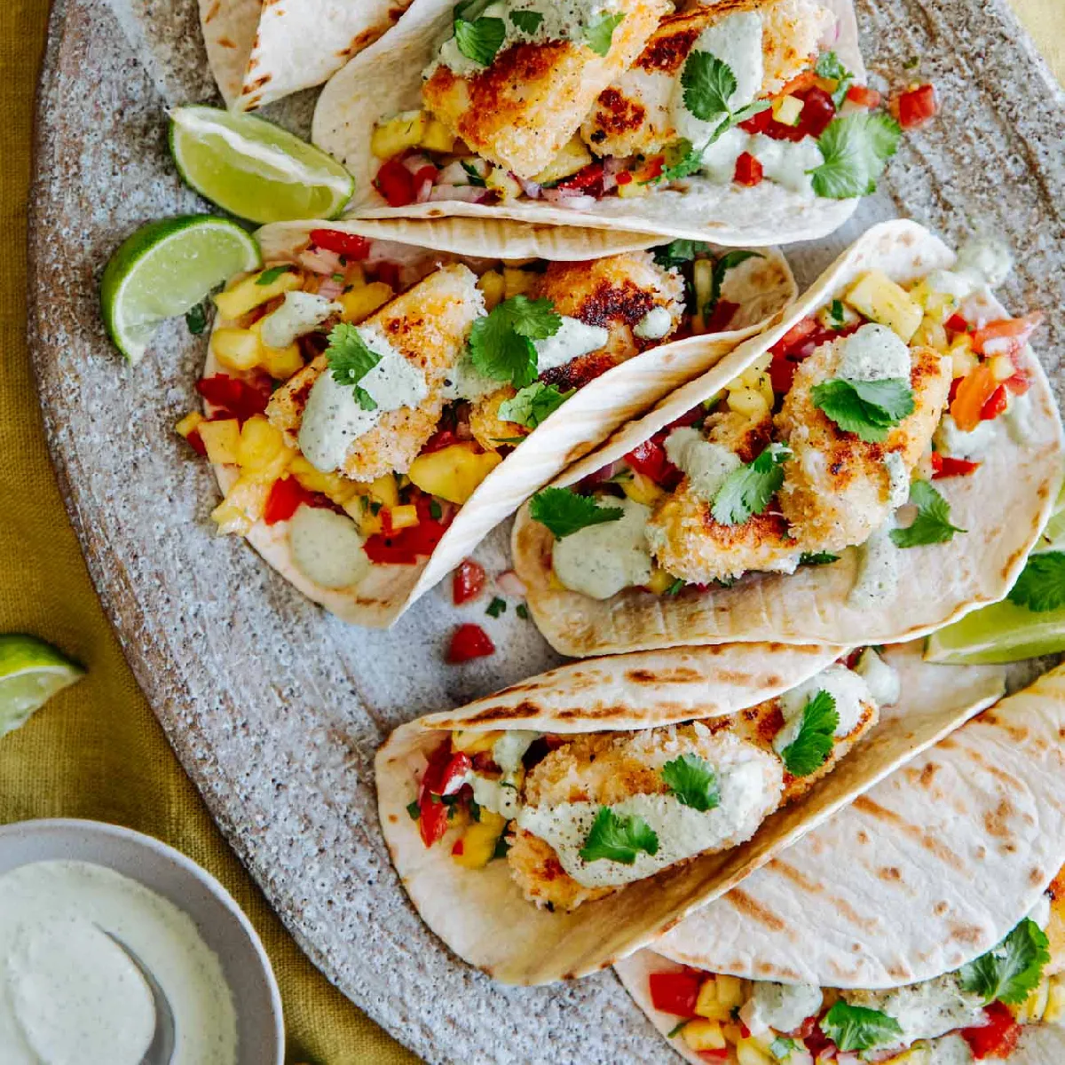 Four delicious fish tacos with crispy fish, colorful salsa, and creamy sauce, garnished with cilantro and lime.