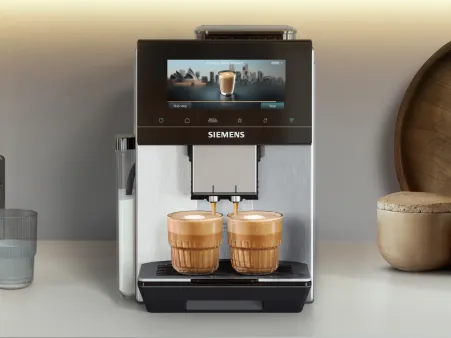 A Siemens coffee machine on a kitchen counter with two wooden cups, glassware, and wooden containers beside it under soft cabinet lighting.