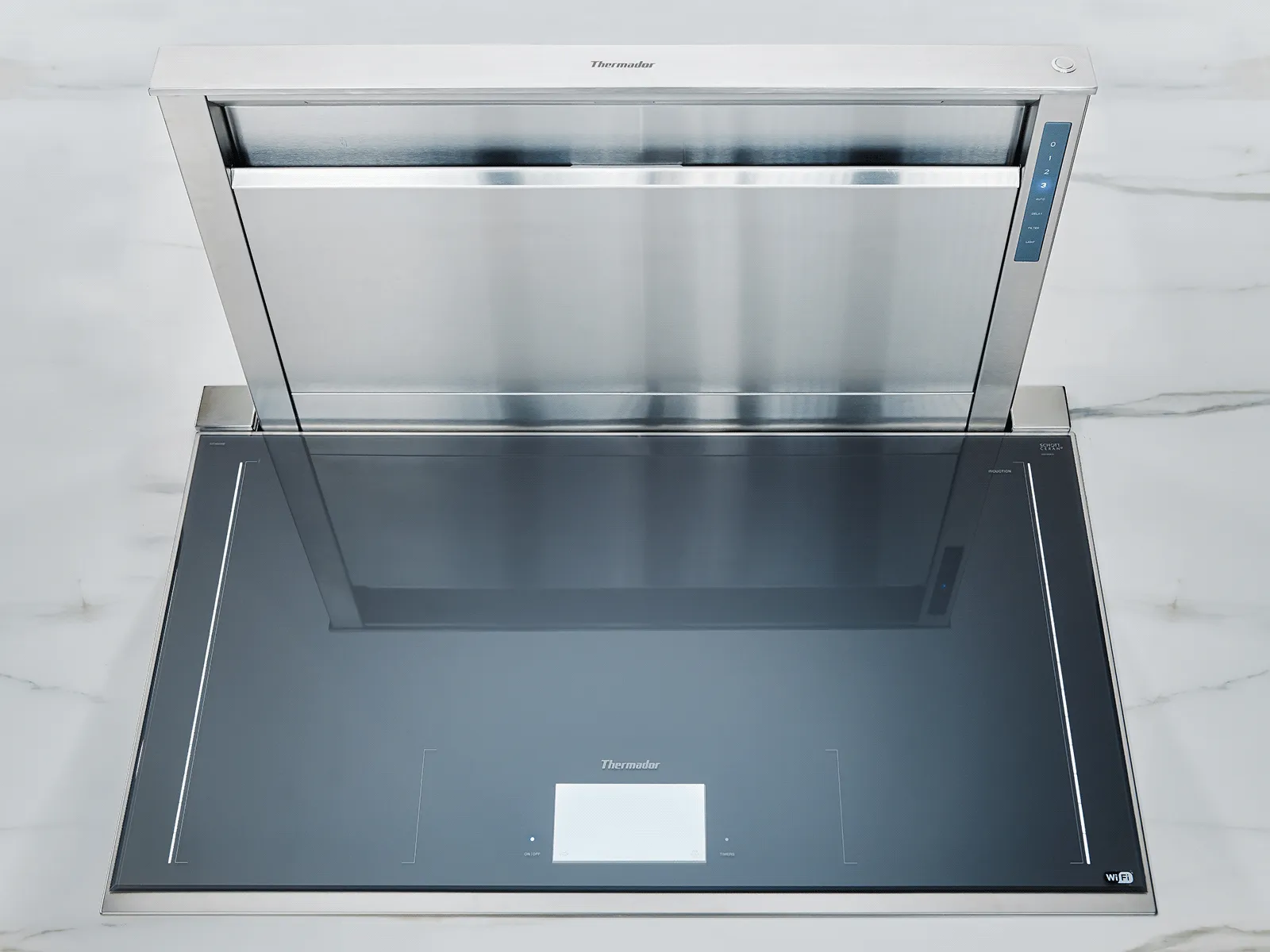 Sleek Thermador built-in induction cooktop with an integrated, retractable stainless steel vent hood on a marble countertop.