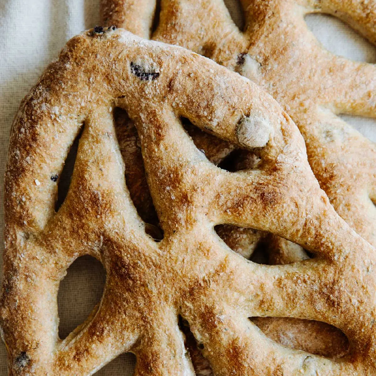 Deux fougasses en forme de feuille avec des trous sont placées sur une surface en tissu de couleur claire.
