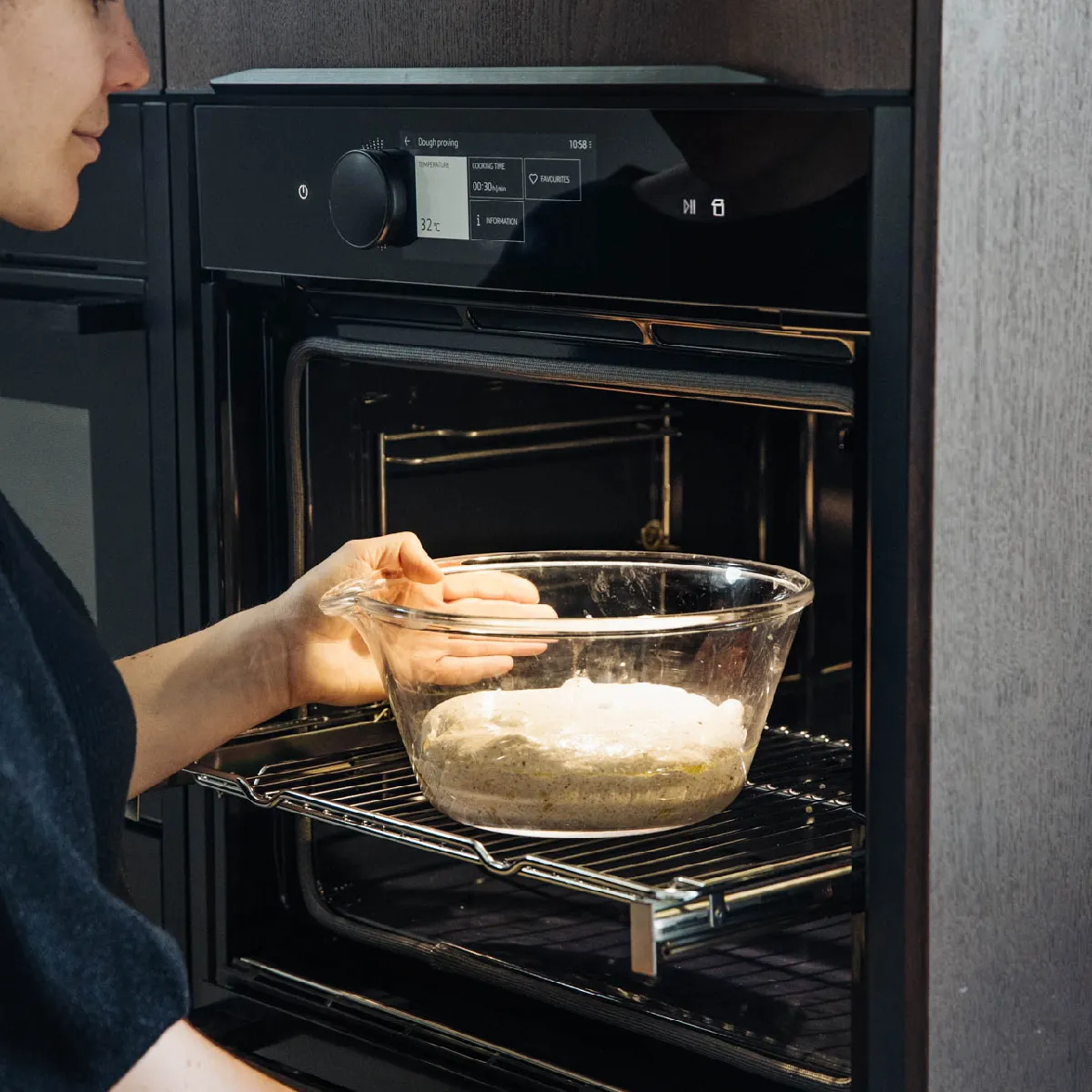Personne plaçant un bol en verre avec de la pâte dans un four moderne réglé à 32°C pour la fermentation de la pâte.
