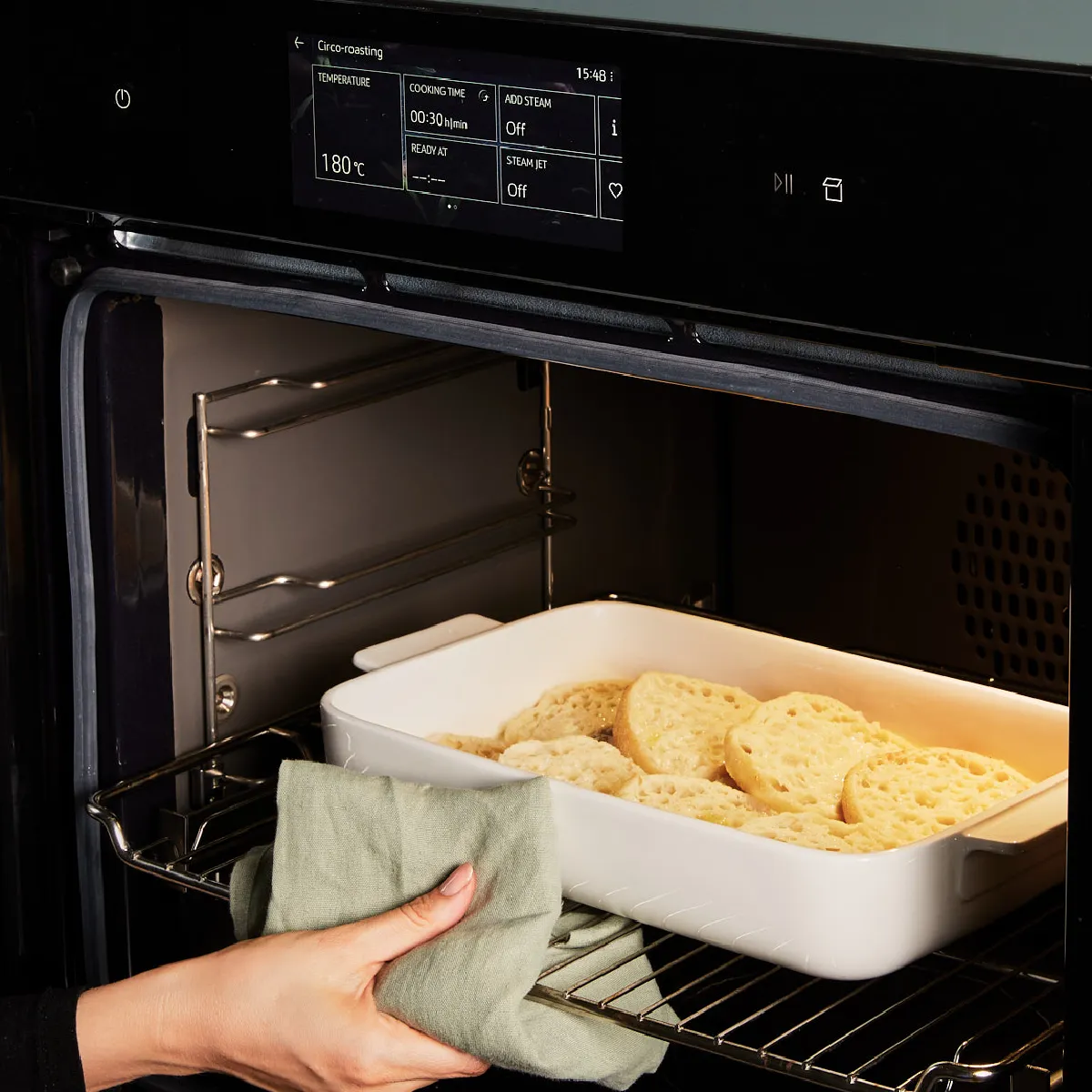 Oven with baked goods, hand reaching in, kitchen appliance, cooking, baking, food preparation.