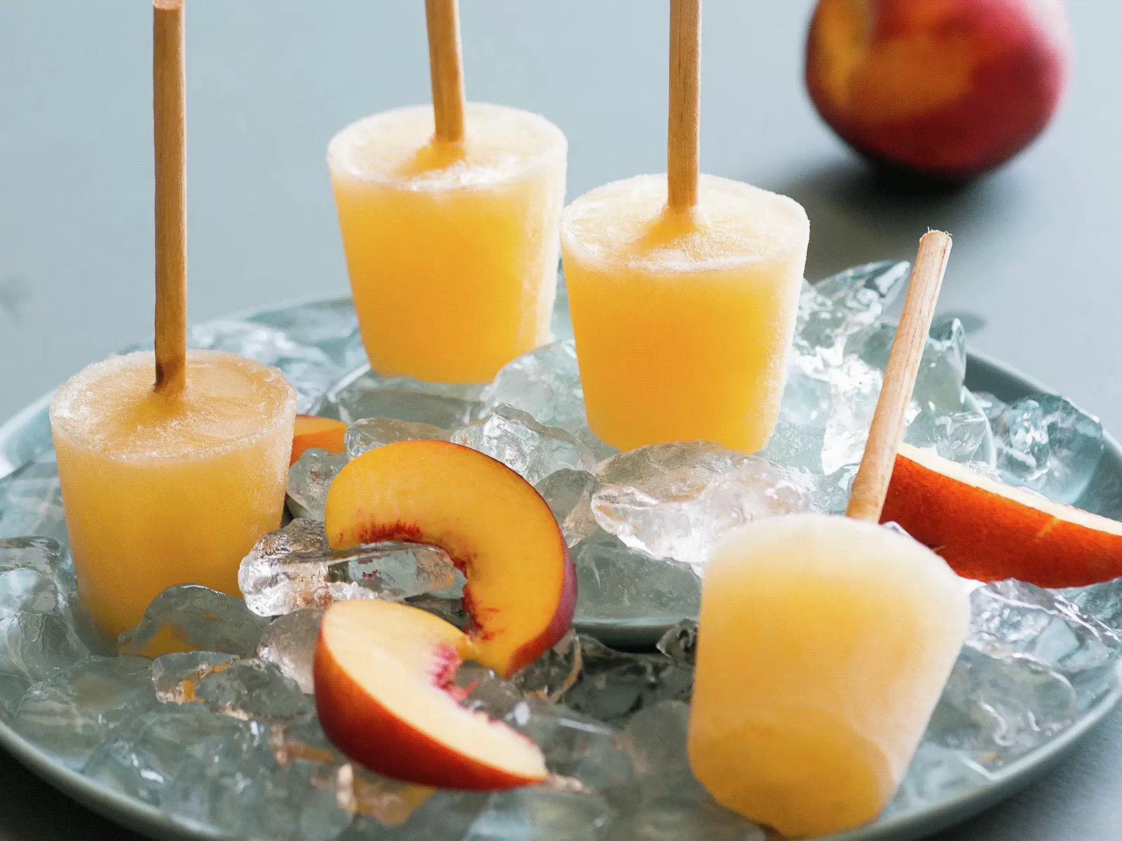 Peach popsicles on a bed of ice with fresh peach slices on a blue plate.