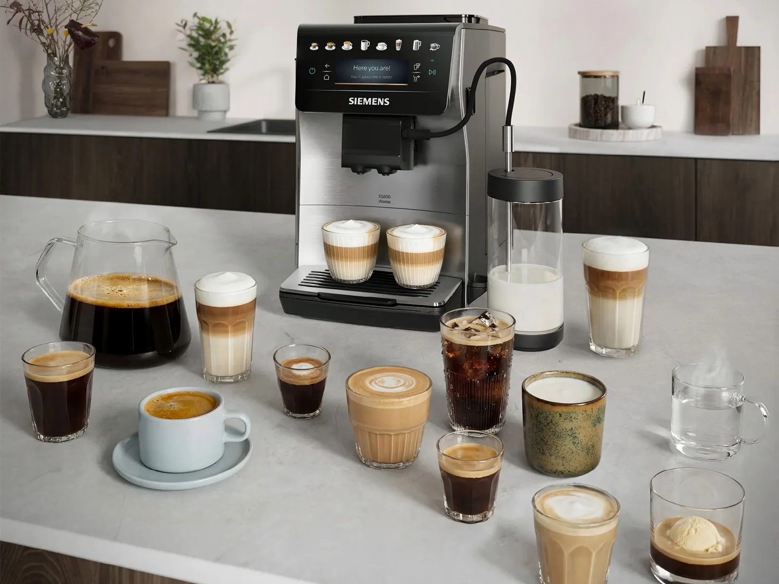 The EQ600 iAroma stands on a kitchen counter surrounded by different coffee beverages.