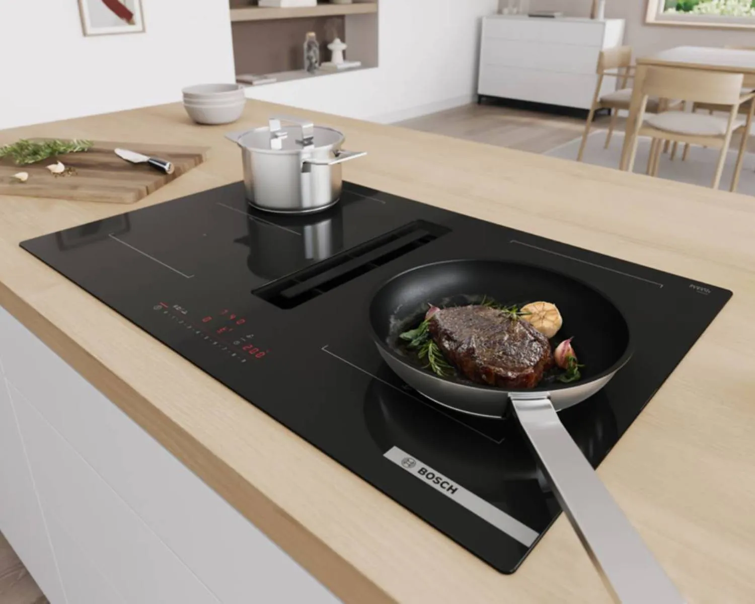 A black Bosch induction cooktop with an integrated downdraft extractor, cooking a steak in a pan and a pot of food, set into a light wooden countertop.
